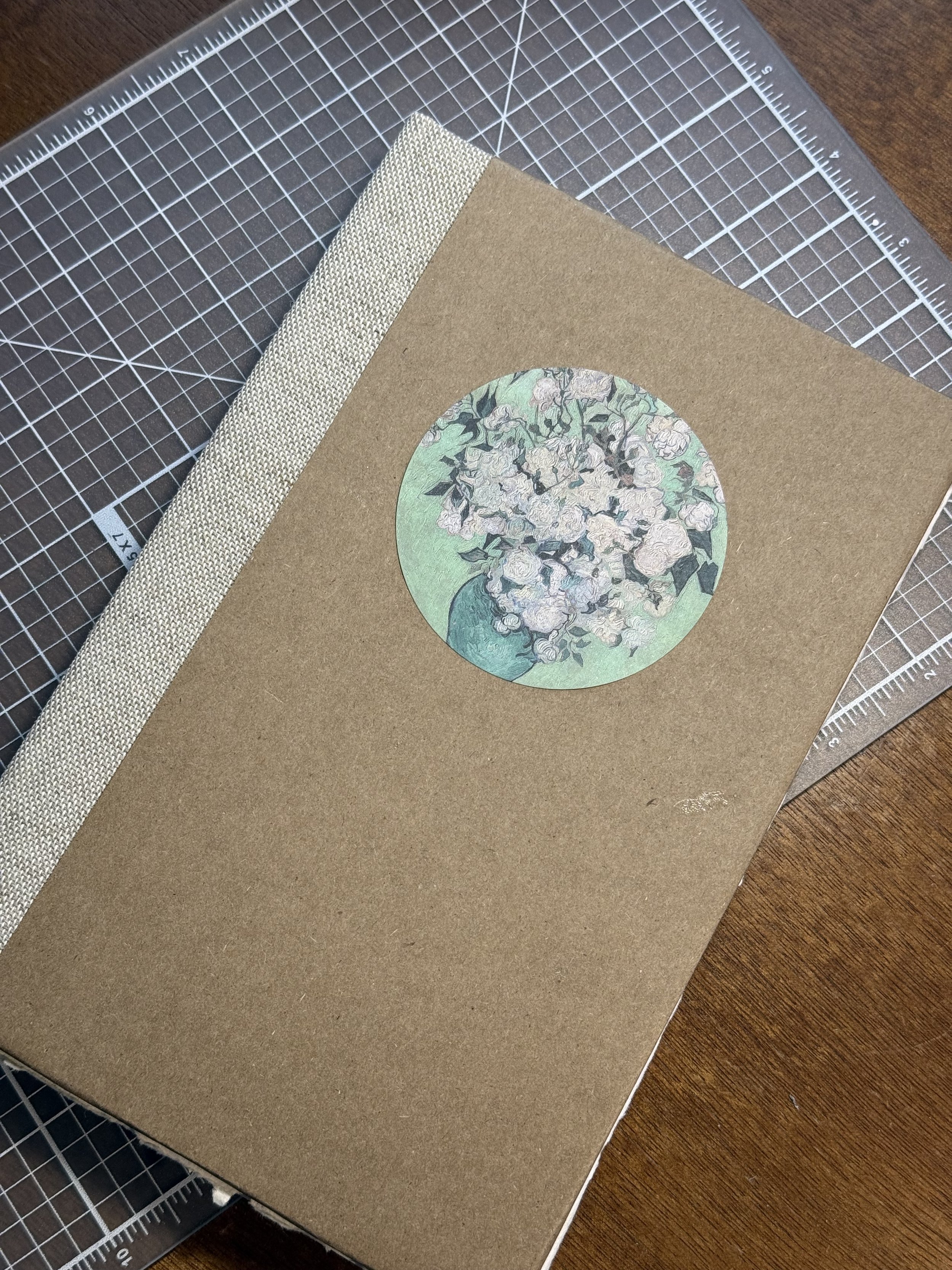 A brown notebook with a floral illustration on the cover, placed on a cutting mat.