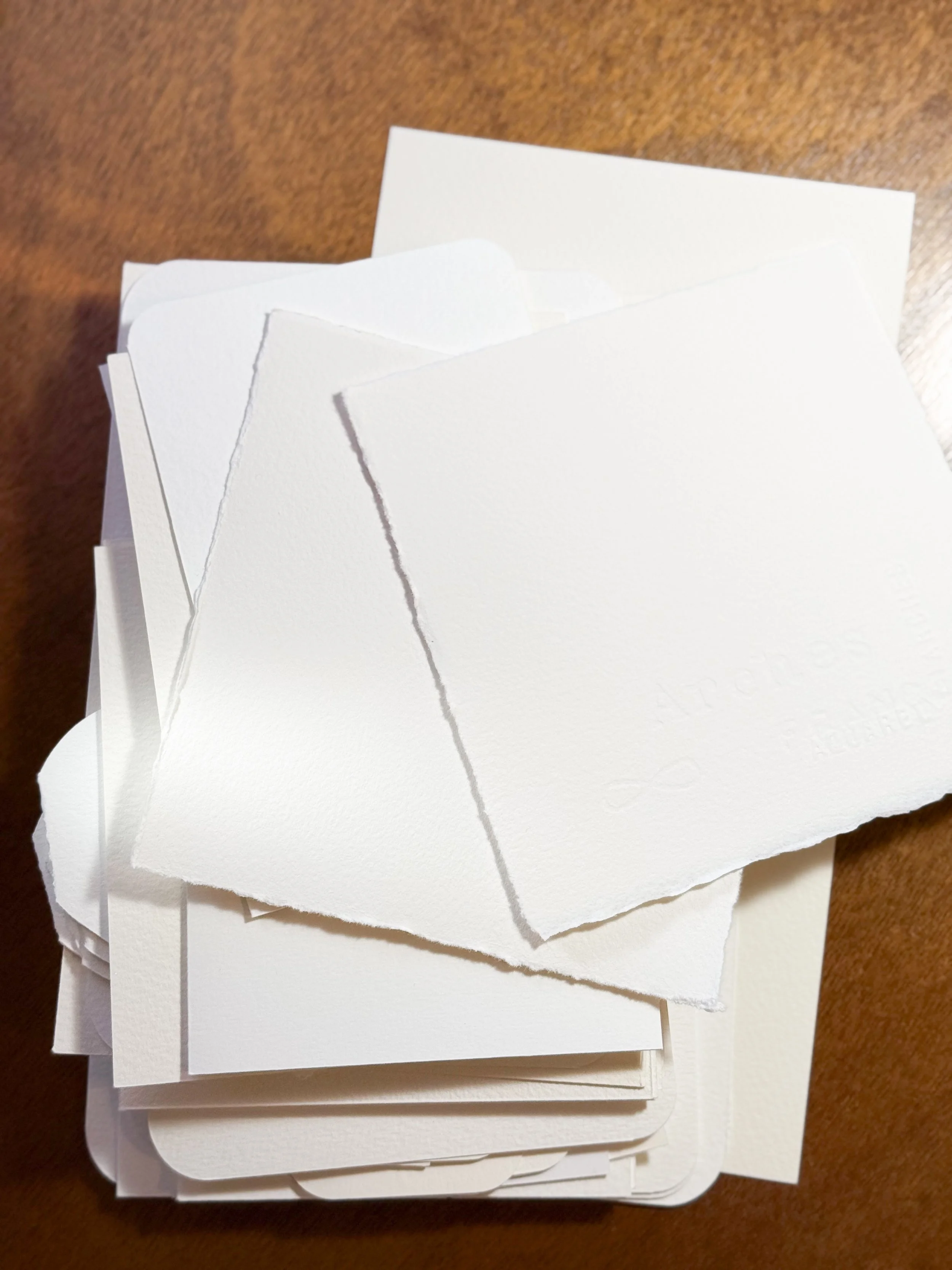 A stack of white, textured paper with a rough, torn edge, placed on a wooden surface.