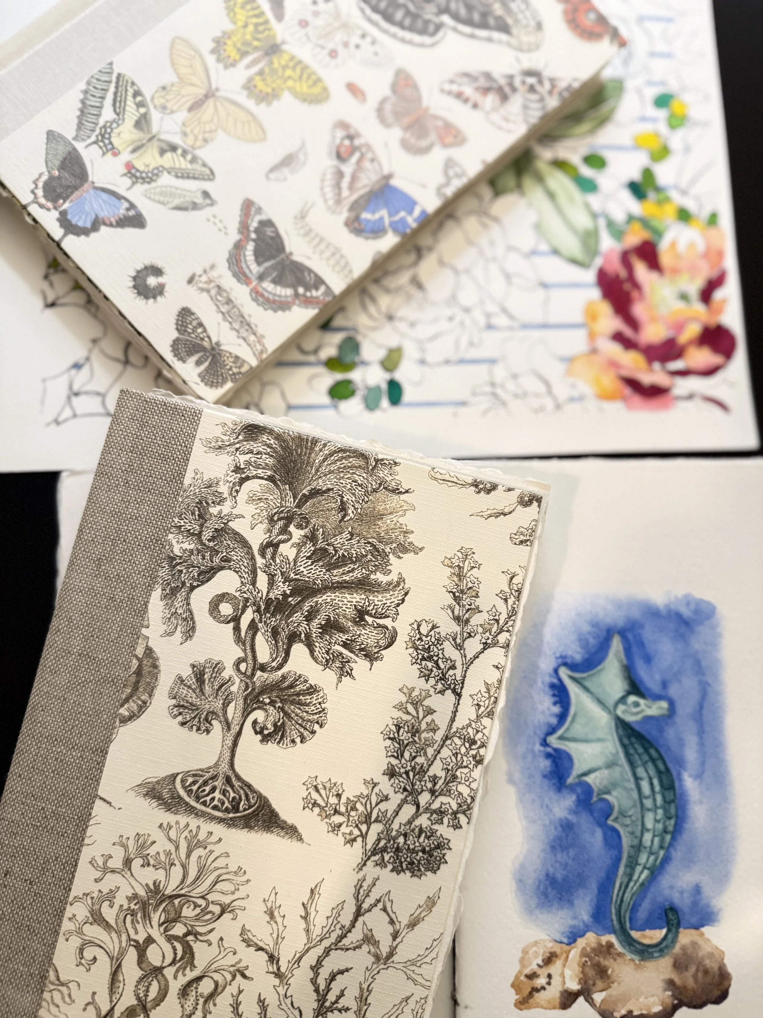 Close-up view of several decorative paper sheets with botanical and animal illustrations, including butterflies, sea horse, and vintage-style trees and plants.