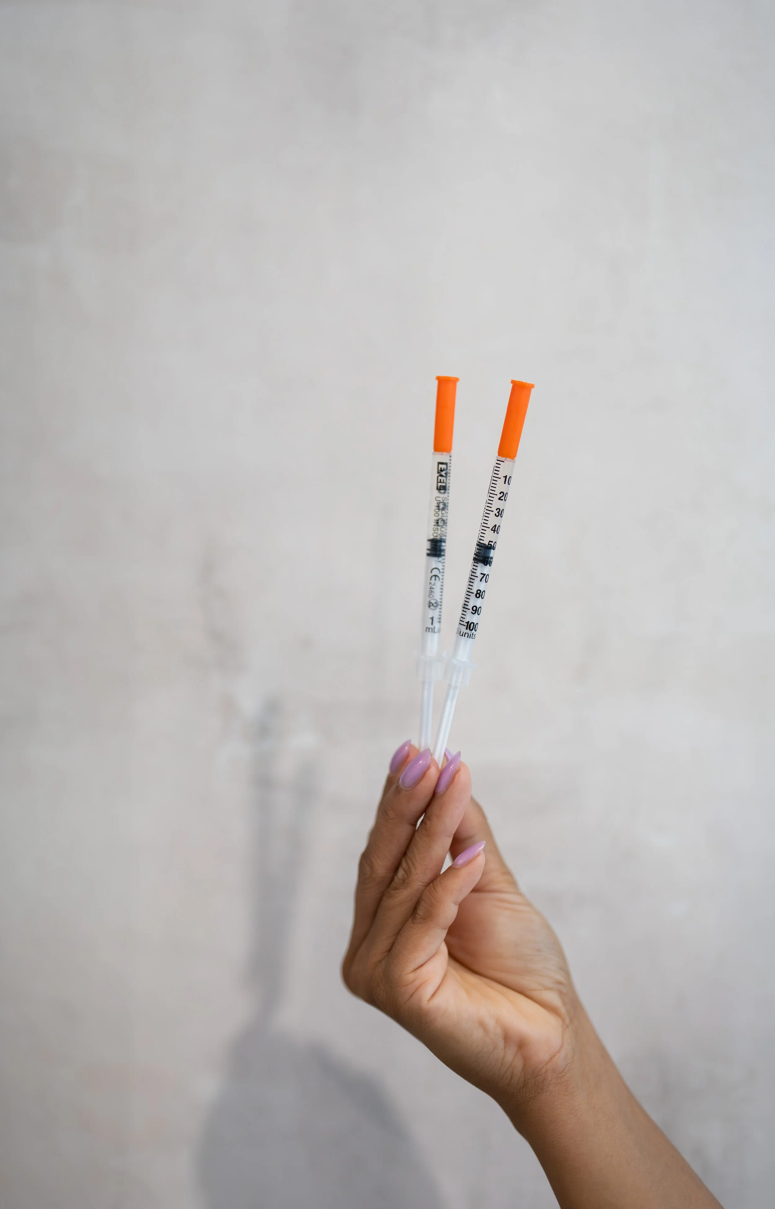Hand holding up medical syringes containing peptides by Kona Health & Aesthetics.