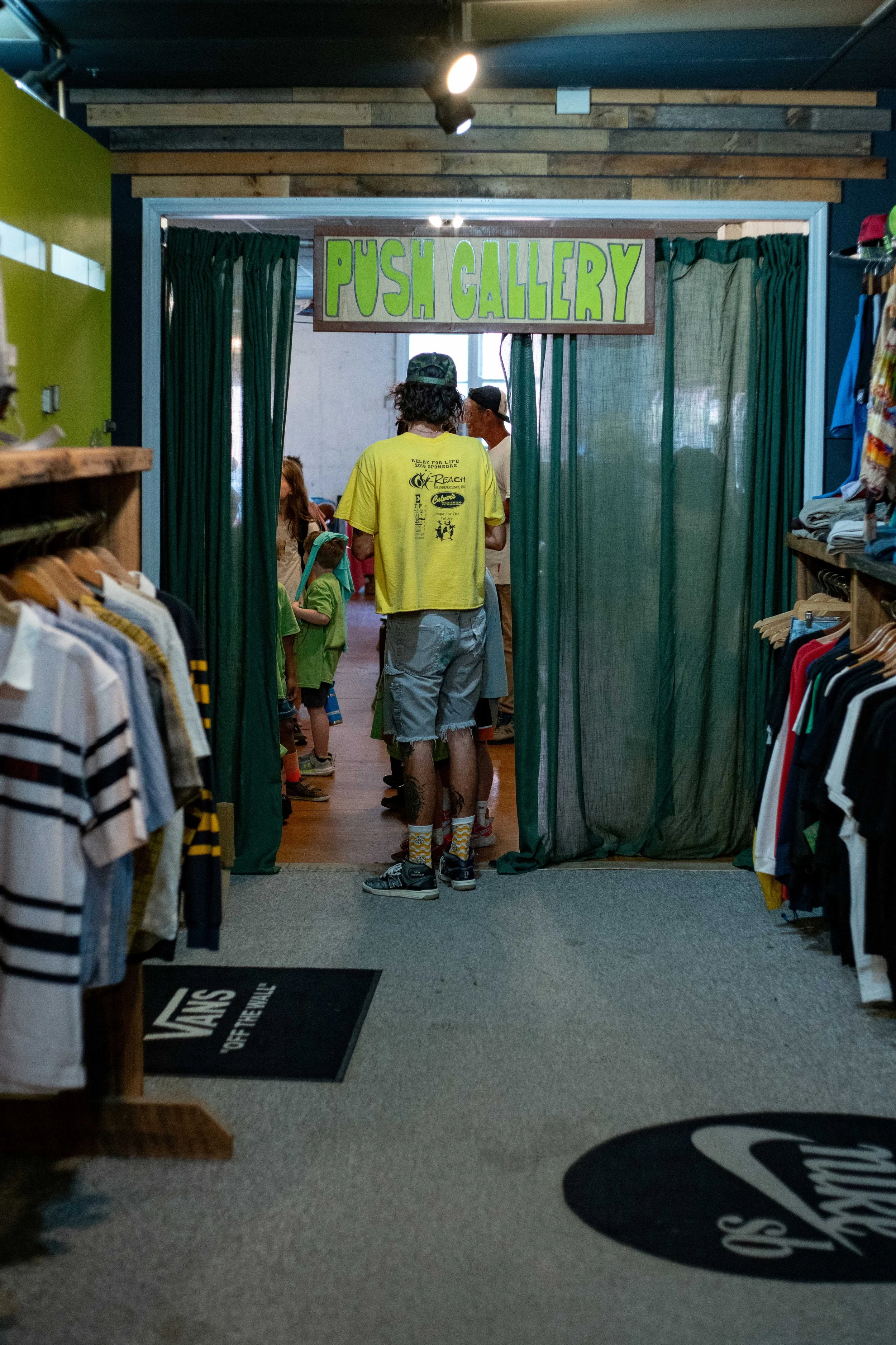 People entering the 'Push Gallery' through a doorway with green curtains inside a retail store.