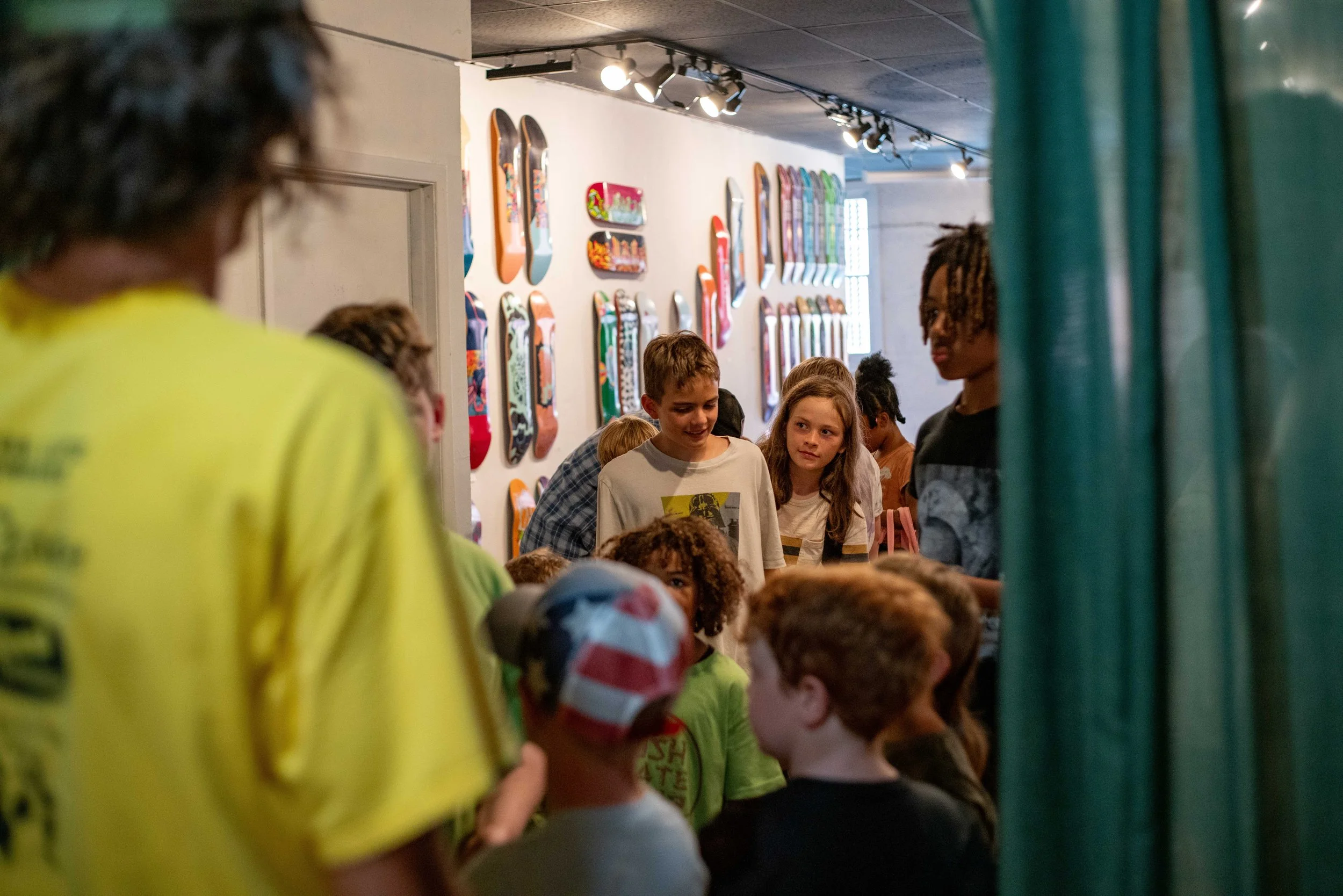 Group of children talking and interacting in a skate shop surrounded by skateboard decks on the wall.