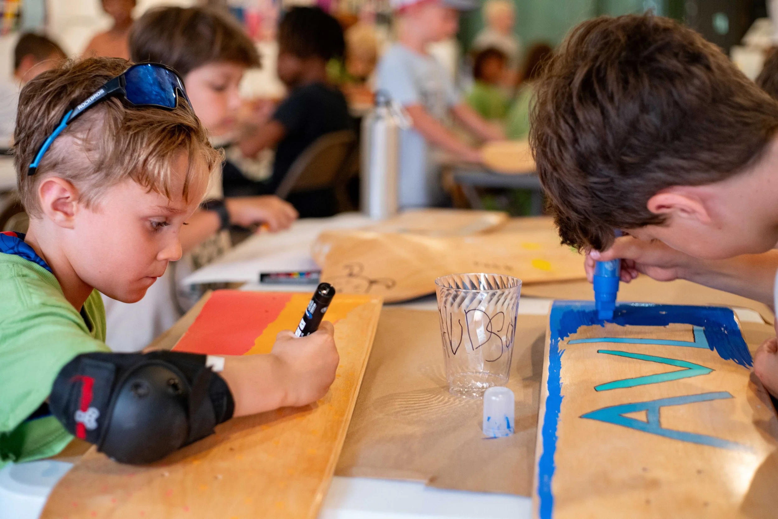 Children painting on wooden boards at a table in a classroom.
