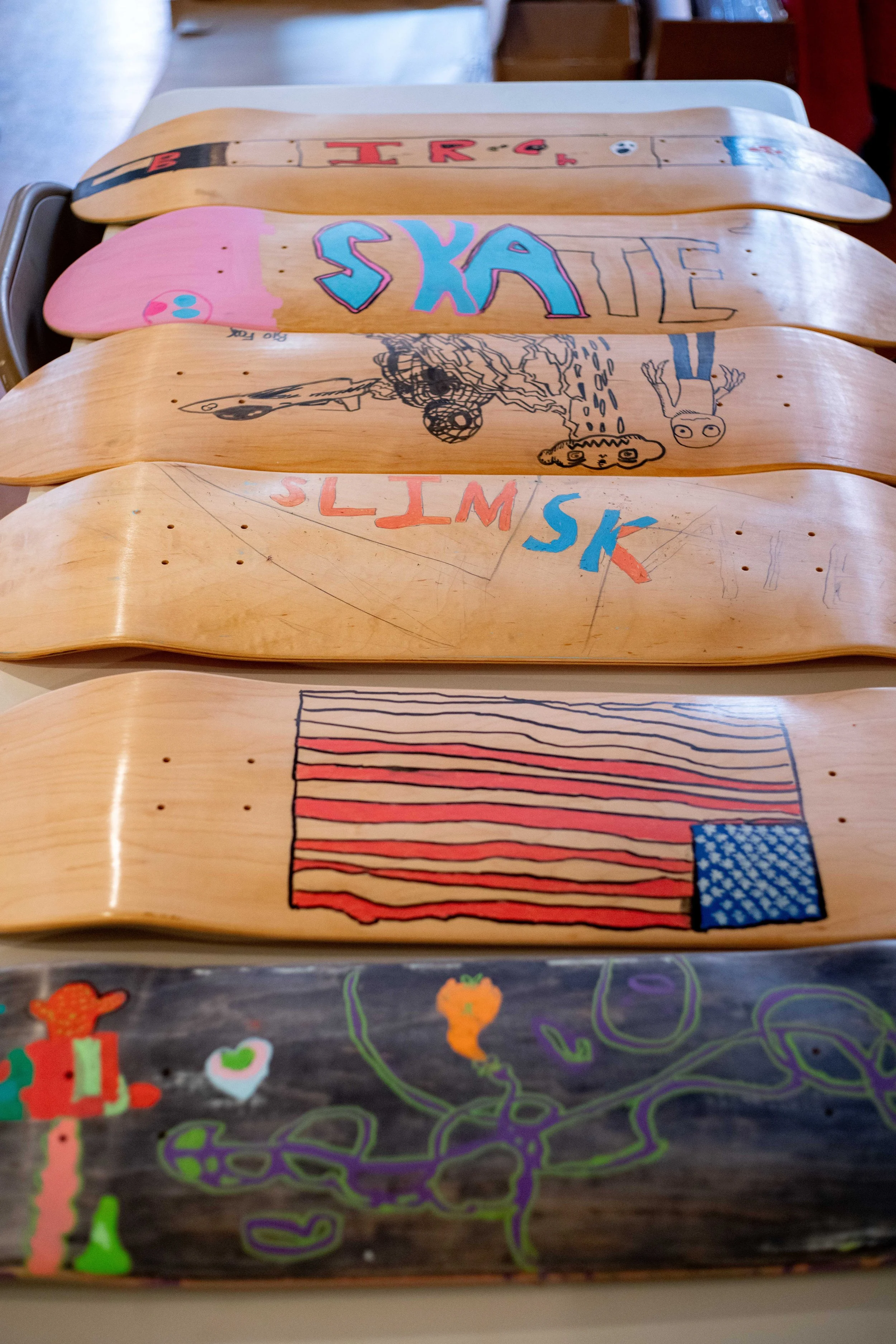 A row of skateboard decks with various colorful designs and artwork, including writing, drawings, and patterns.