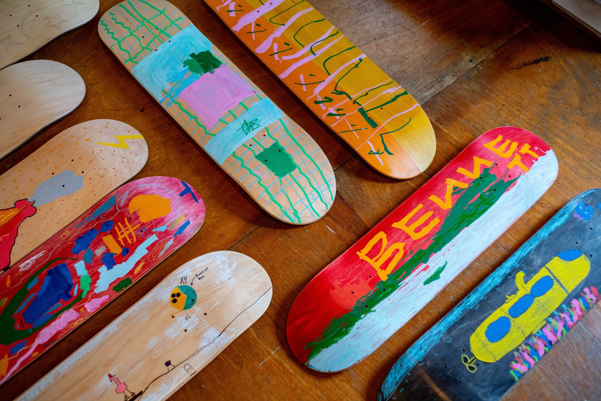 Collection of painted skateboard decks with colorful abstract and graffiti-style designs on a wooden surface.