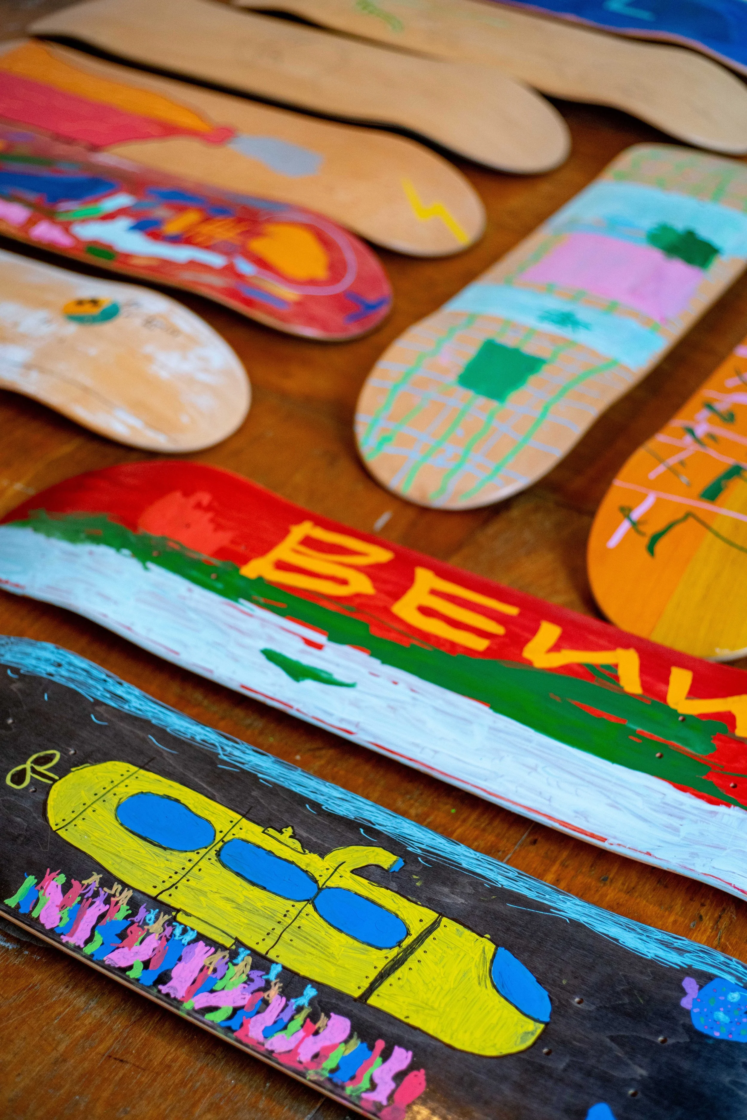 Colorfully painted wooden skateboards with various designs arranged on a wooden surface.
