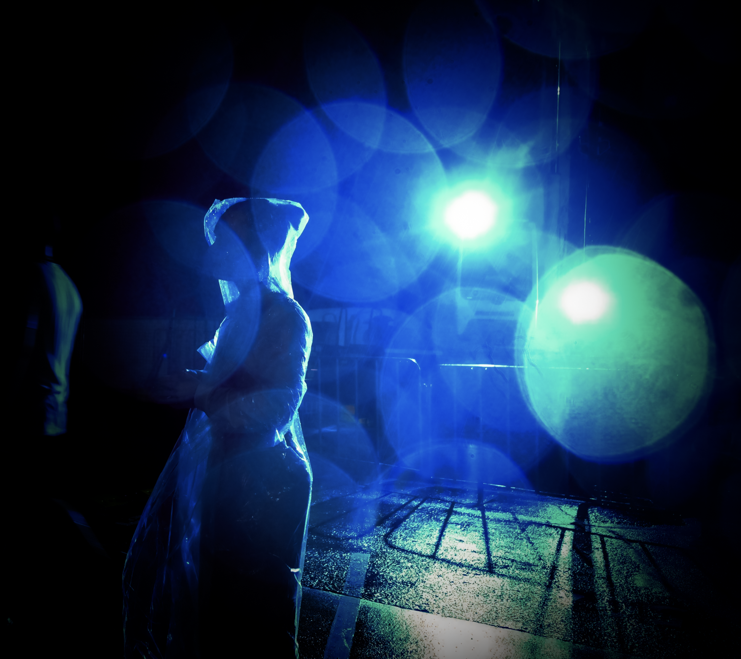 Bondi Chanukkah. Person wearing a raincoat under bright blue stage lights in a dark setting.