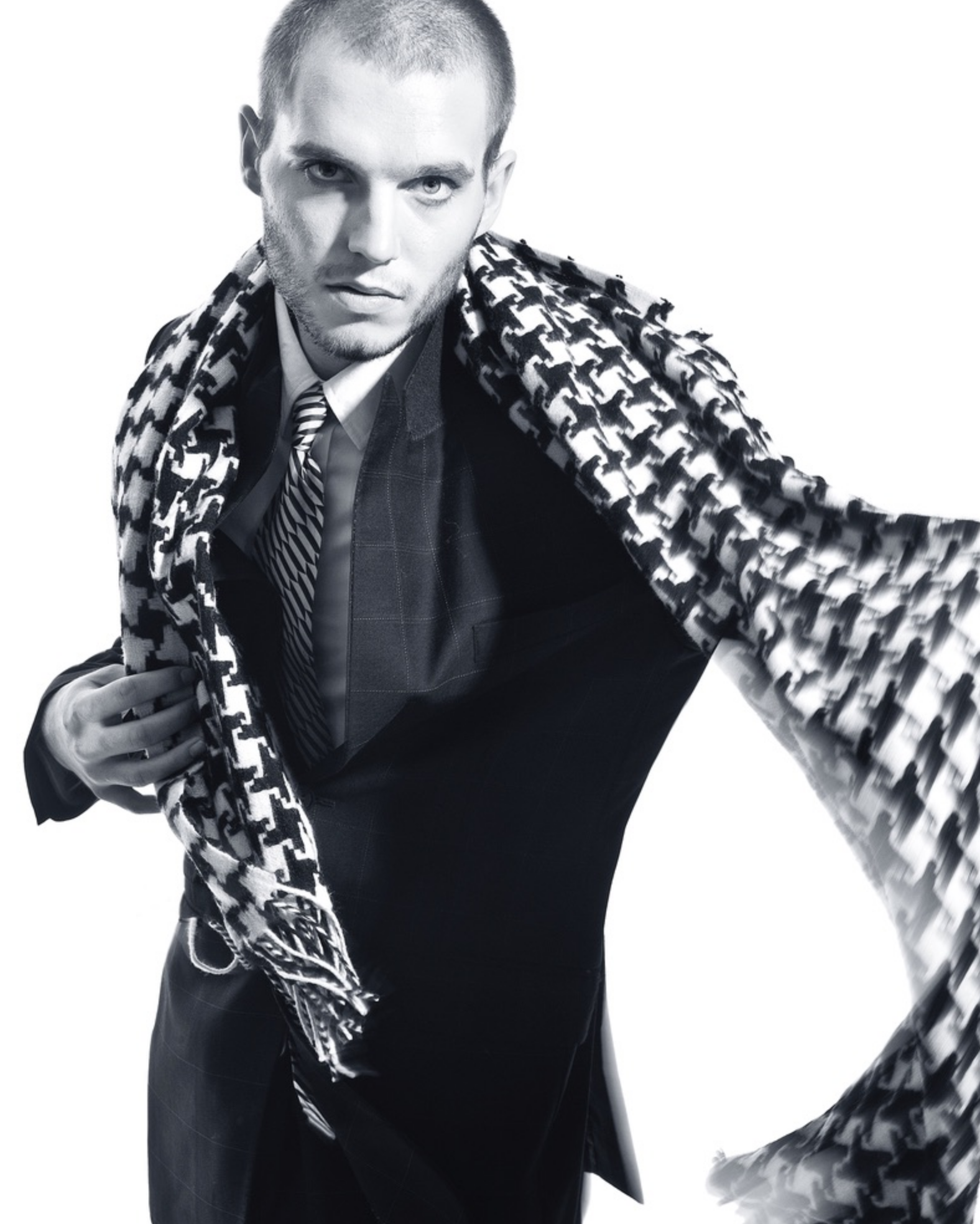 A man in a suit holding a patterned scarf over his shoulders, looking directly at the camera against a white background.