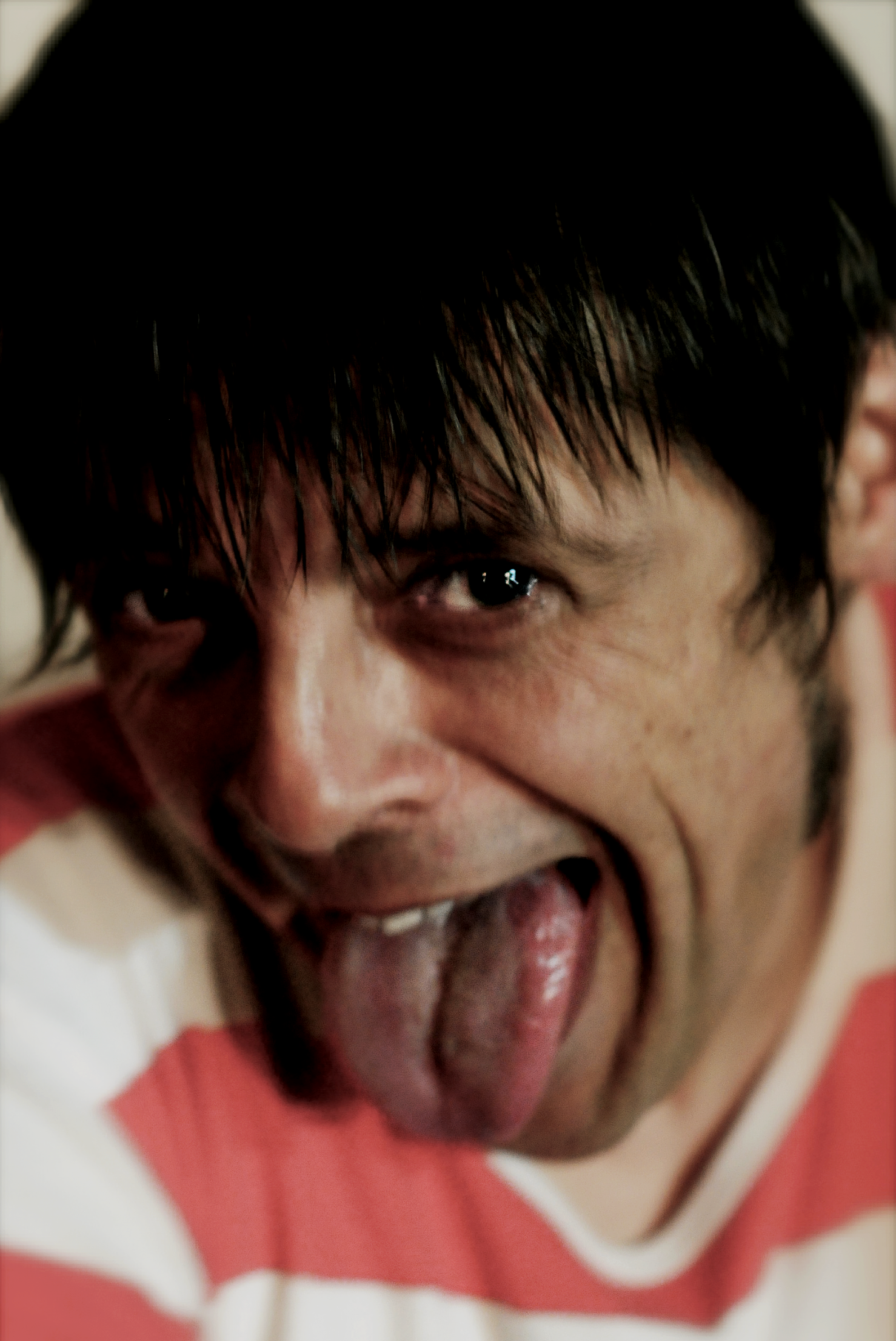 Primal Scream, Mani, Bobby Gillespie, Fuji Rock Festival, A person with wet, dark hair sticking to their forehead, making a face with one eye open, tongue sticking out, and a playful expression.