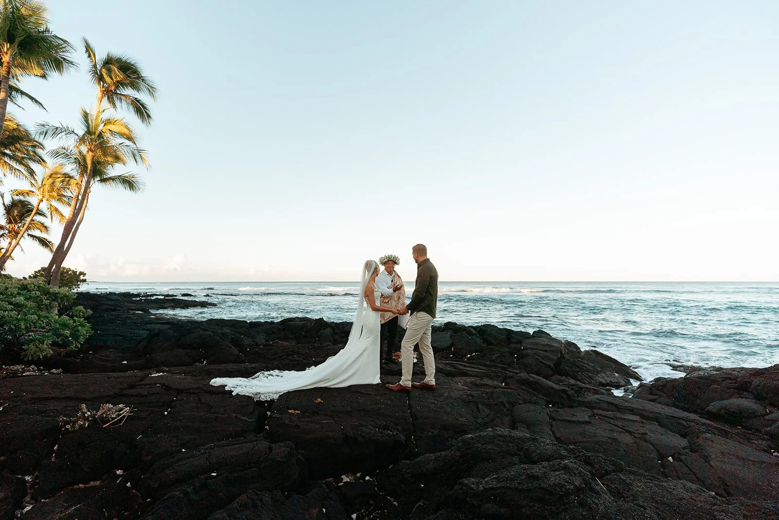 Couple celebrating their wedding ceremony on a lava-rock coastline on the Big Island of Hawaii.