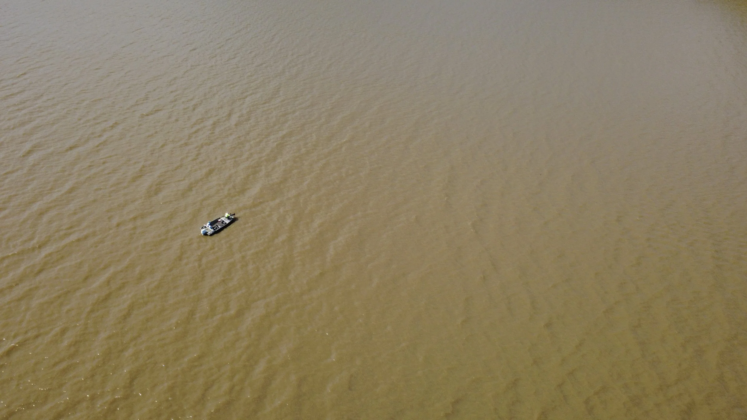 An aerial view of a small boat on muddy brown water.