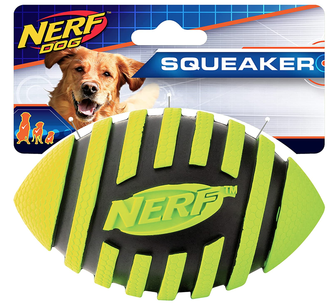 A Nerf Dog Squeaker toy designed for dogs, shaped like a football, yellow and black with a Nerf logo, in front of its packaging featuring a picture of a happy dog.