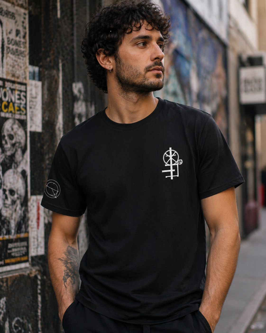 Male model wearing black crew neck t-shirt  with minimal white graphic on the chest. The graphic appears to be a mechanical engineering symbol design.