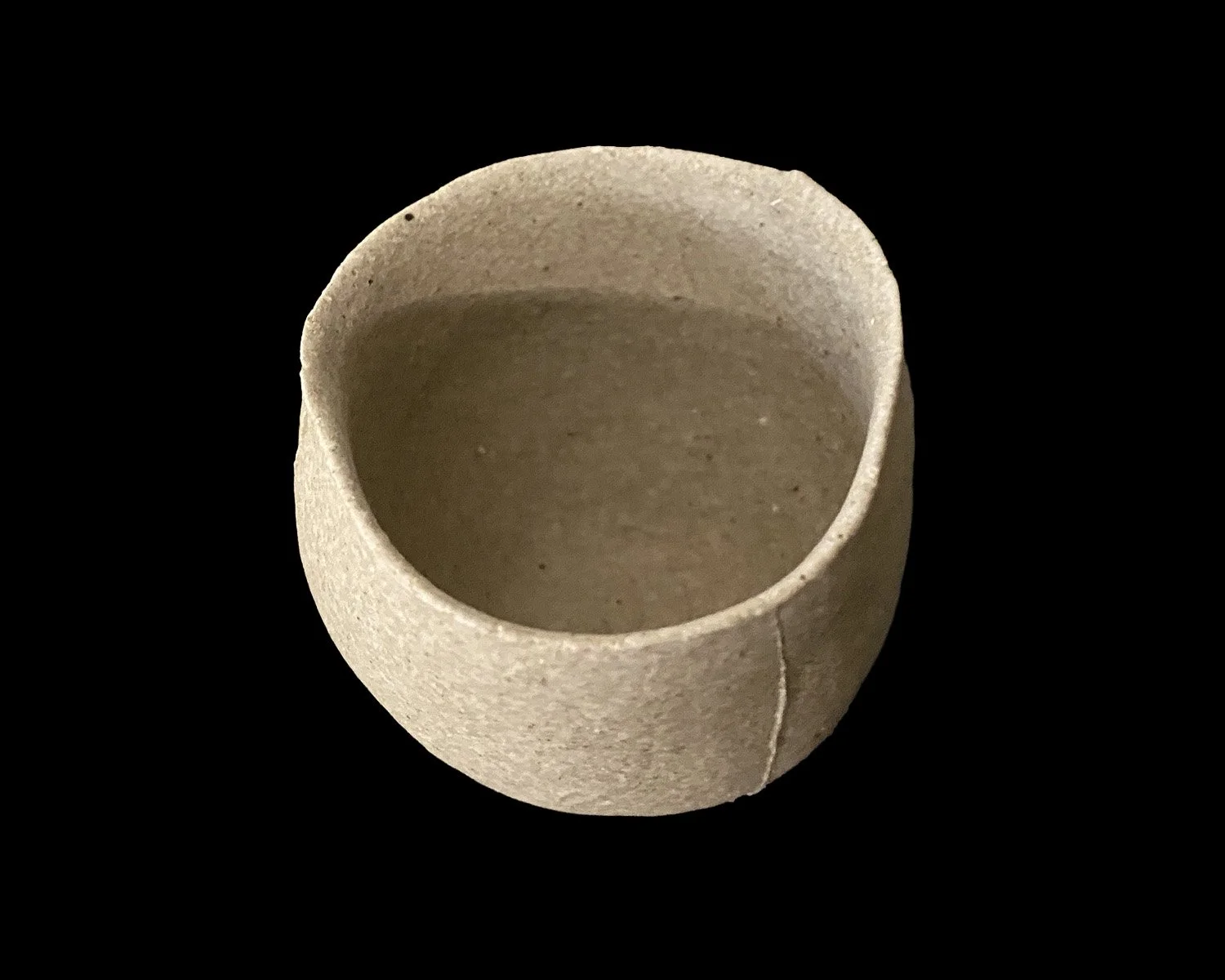Handmade yakishime unglazed stoneware cup isolated on a black background showing natural clay texture