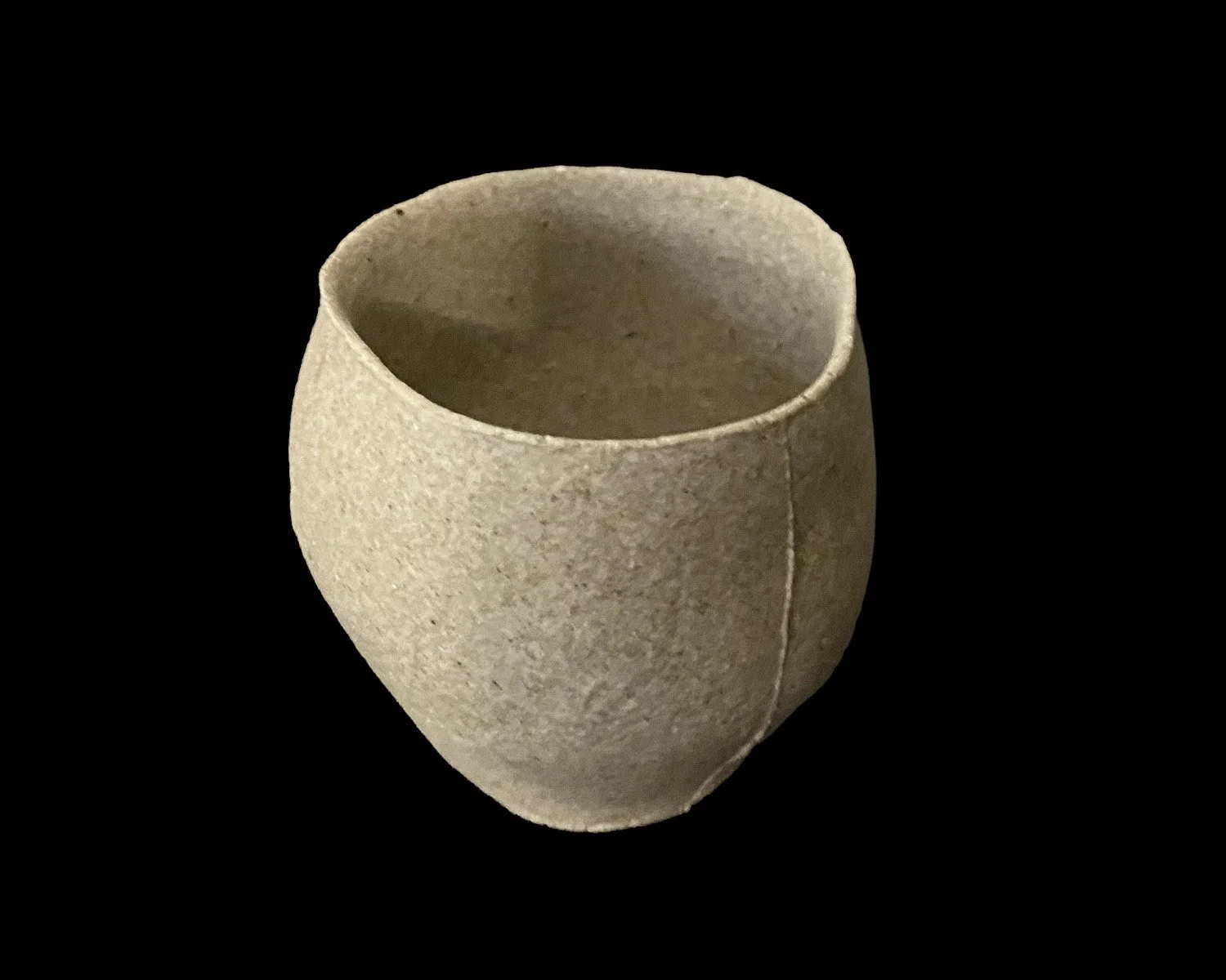 Handmade yakishime unglazed stoneware cup isolated on a black background showing natural clay texture