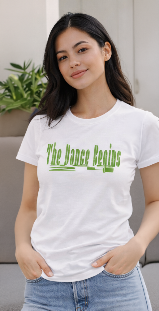 White t-shirt with the text "The Dance Begins" in green, paired with blue jeans. The image shows a person wearing sunglasses and holding a drink, set against a city skyline at sunset.