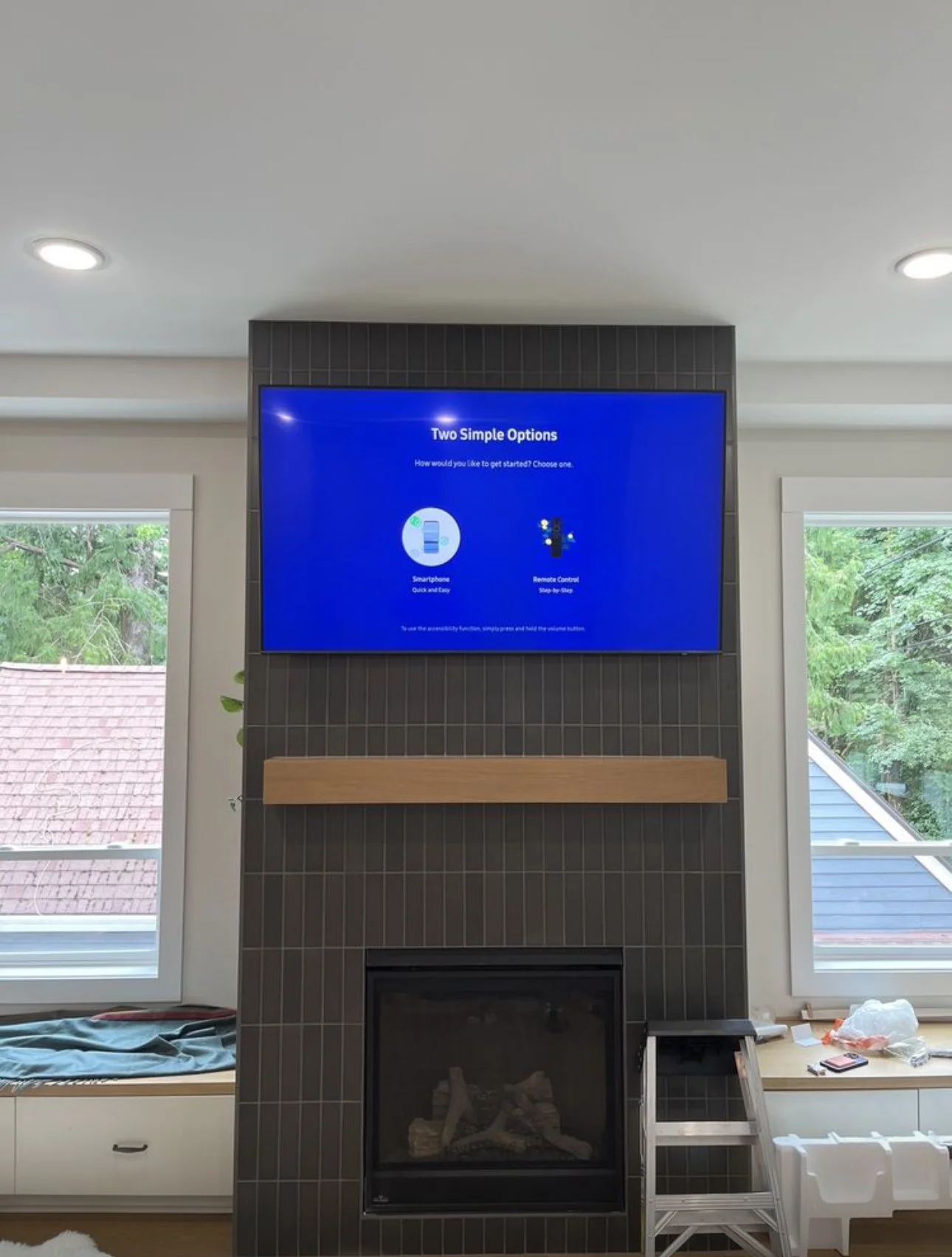 A television screen displaying two options on how to get started, with a fireplace below and windows on either side showing trees outside.