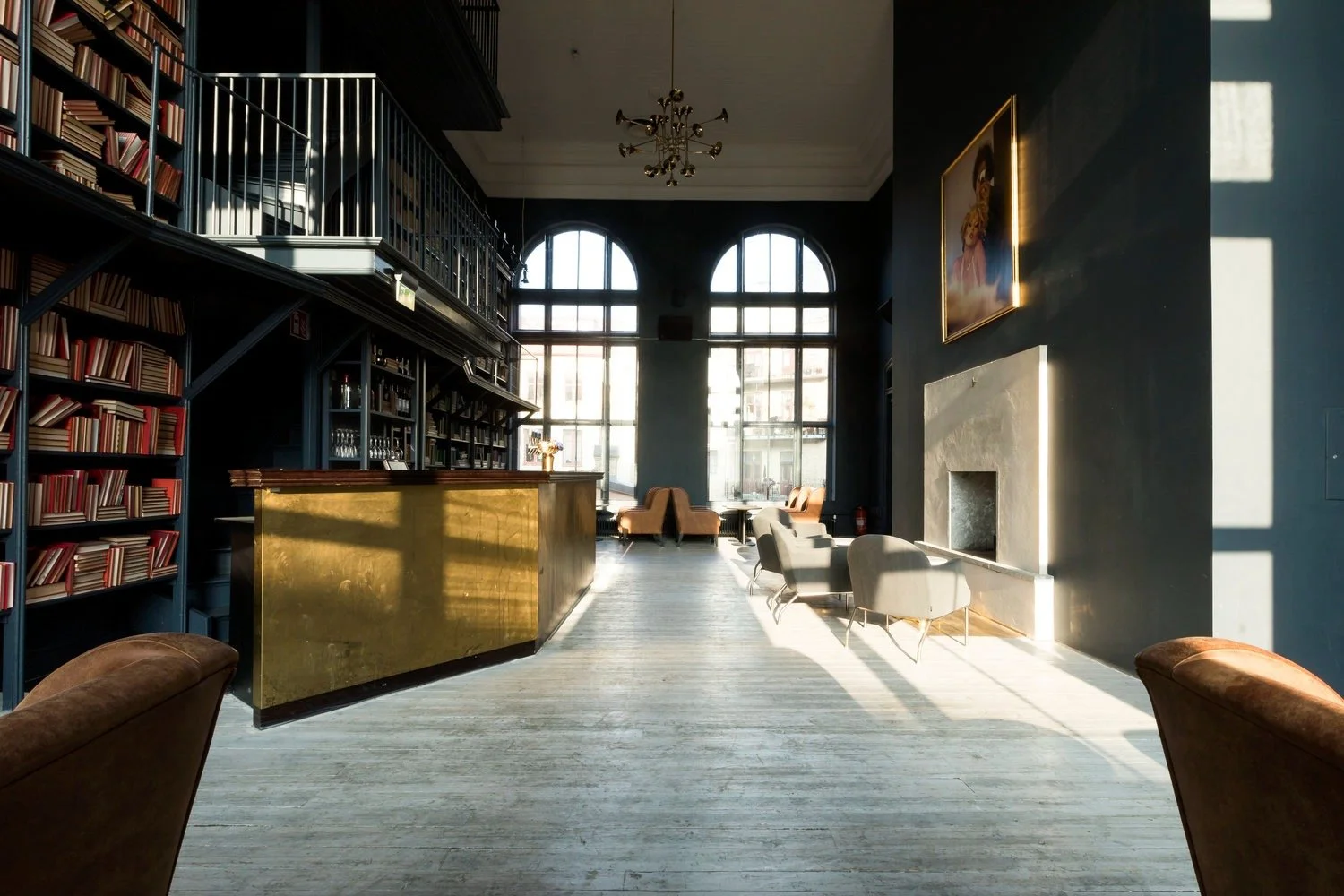 Interiör av ett ljust bibliotek eller lounge med stora fönster, bokhyllor, soffor och stolar