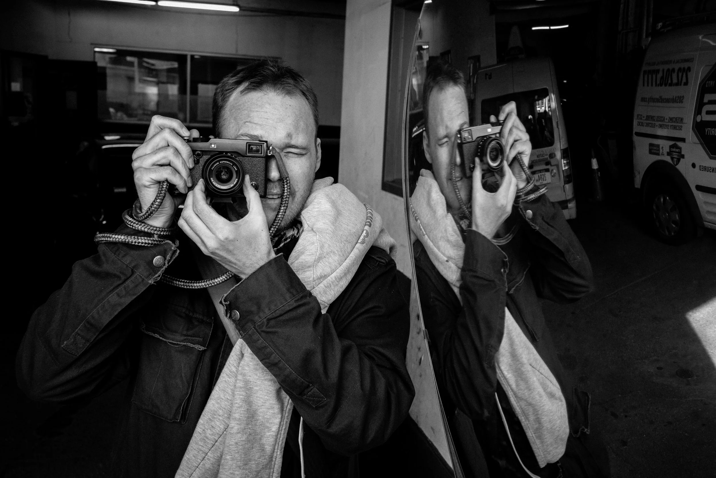 A black and white photo of a man using a camera with a Sailor Strap made of rope and leather. The strap adds a nautical touch to the classic image.