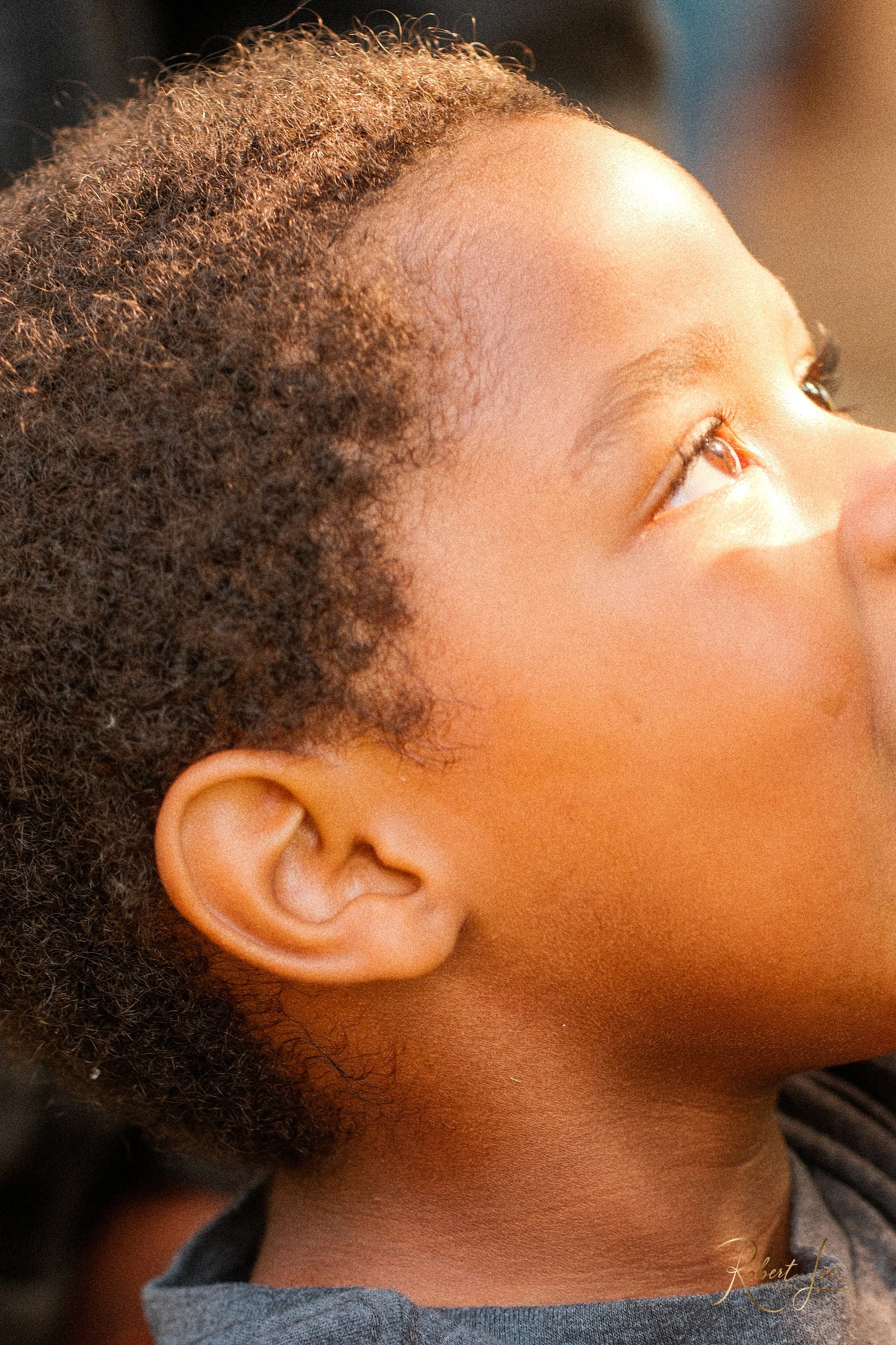 Close-up of a young girl's face, showing her left eye, ear, and part of her cheek and neck, with natural curly hair framing her face.