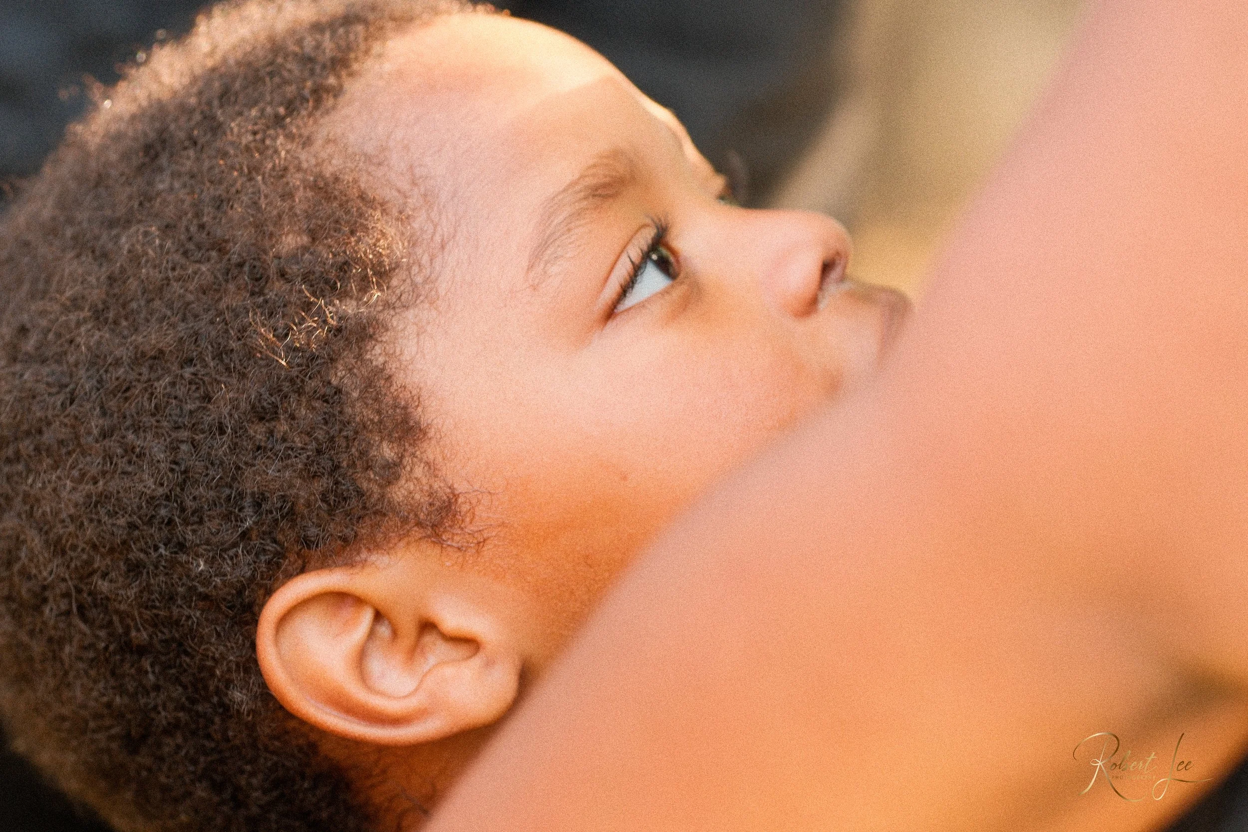 Close-up of a young child with curly hair lying on their back, looking upwards.