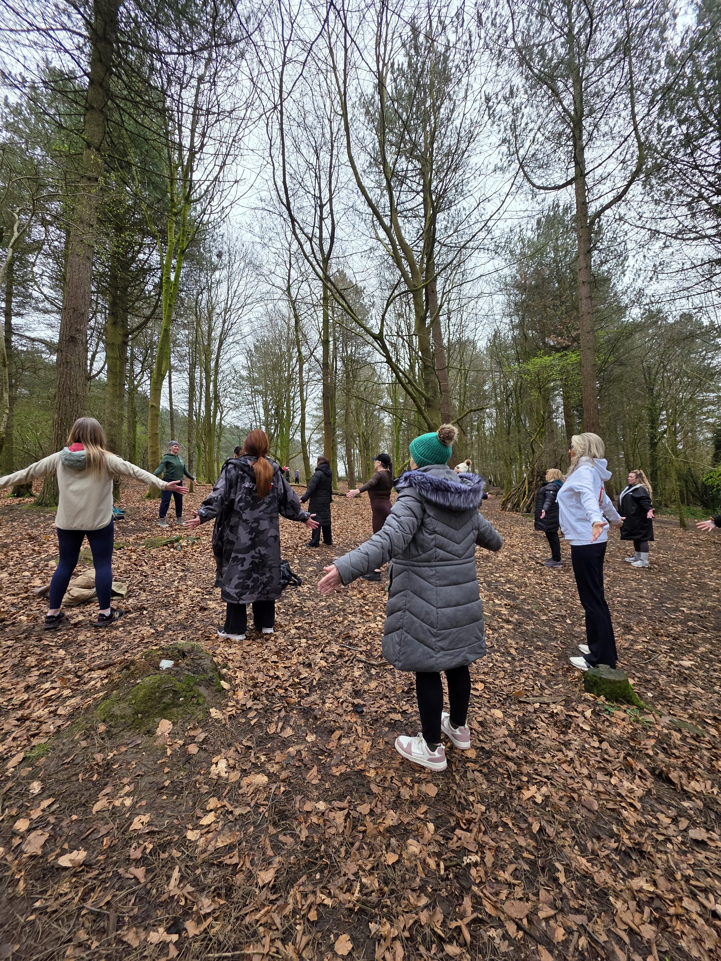 Group of people standing in a circle in a wooded area, participating in an outdoor activity during overcast weather.