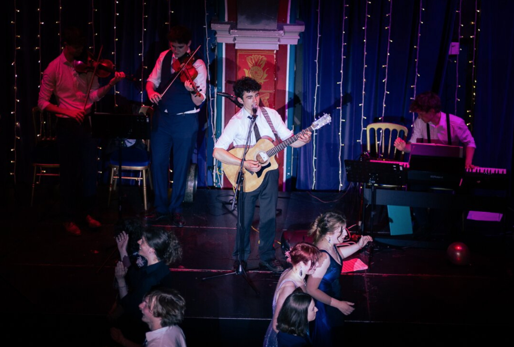Ceilidh band with guitarist singing on a stage in the spotlight. people dancing on the floor in front of them