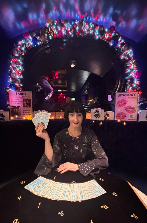 Ellie Velvet, holding tarot cards with a spread of them laid on a table in front of her.