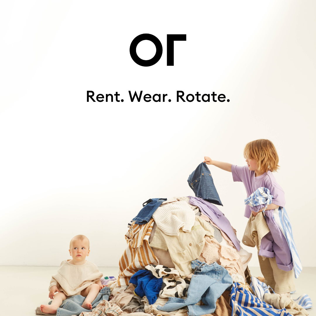 Two young children playing with a large pile of mixed laundry in a plain white room.