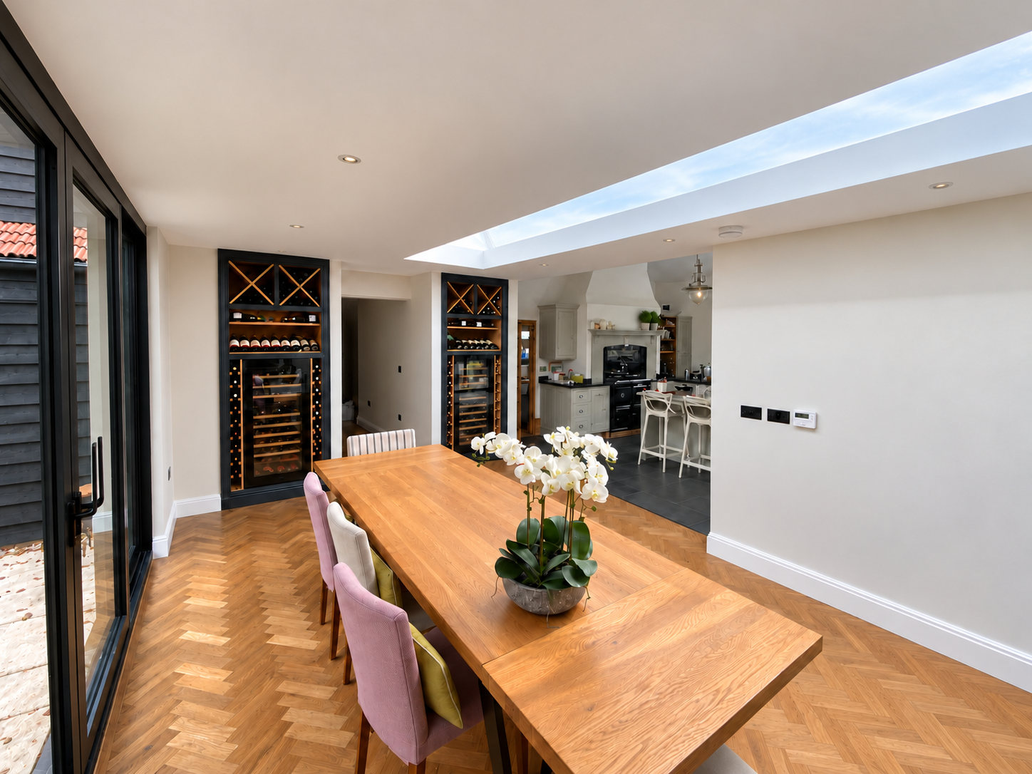 Completed single-storey extension at The Barn, Essex: dining room with herringbone oak floor, full-length rooflight and glazed sliding doors, opening to the kitchen