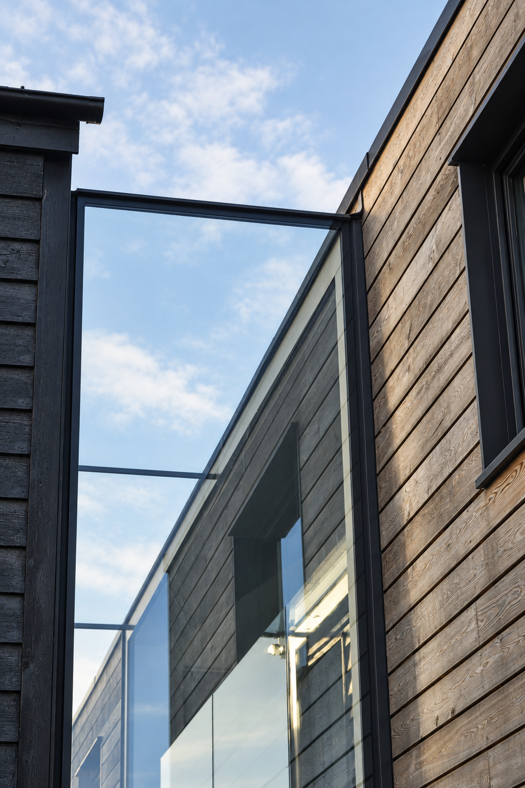 Frameless glass link joining the black weatherboarded barn to the timber-clad extension at Little Nuntys