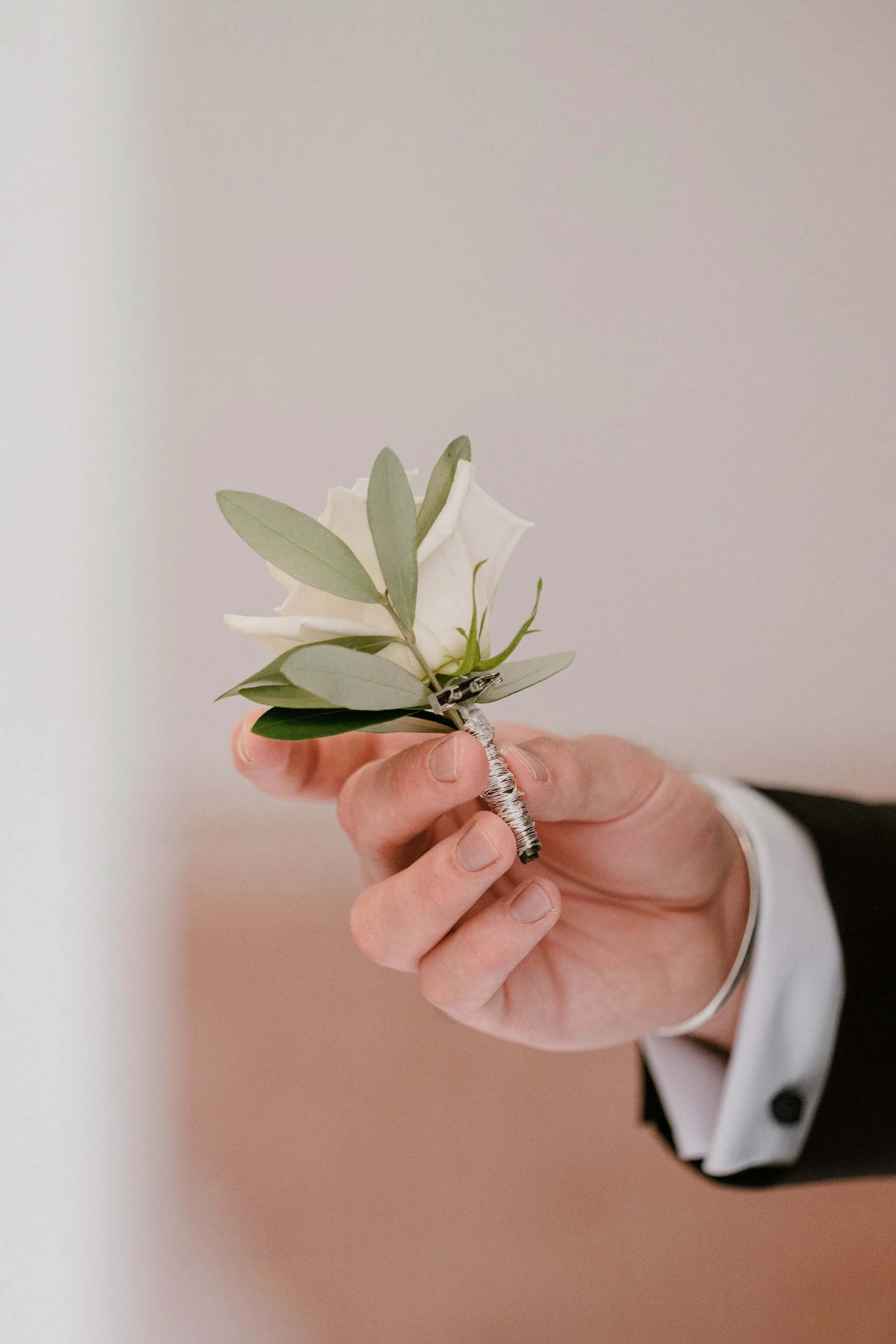 Une main tenant une épinglette avec une petite fleur blanche et des feuilles vertes.