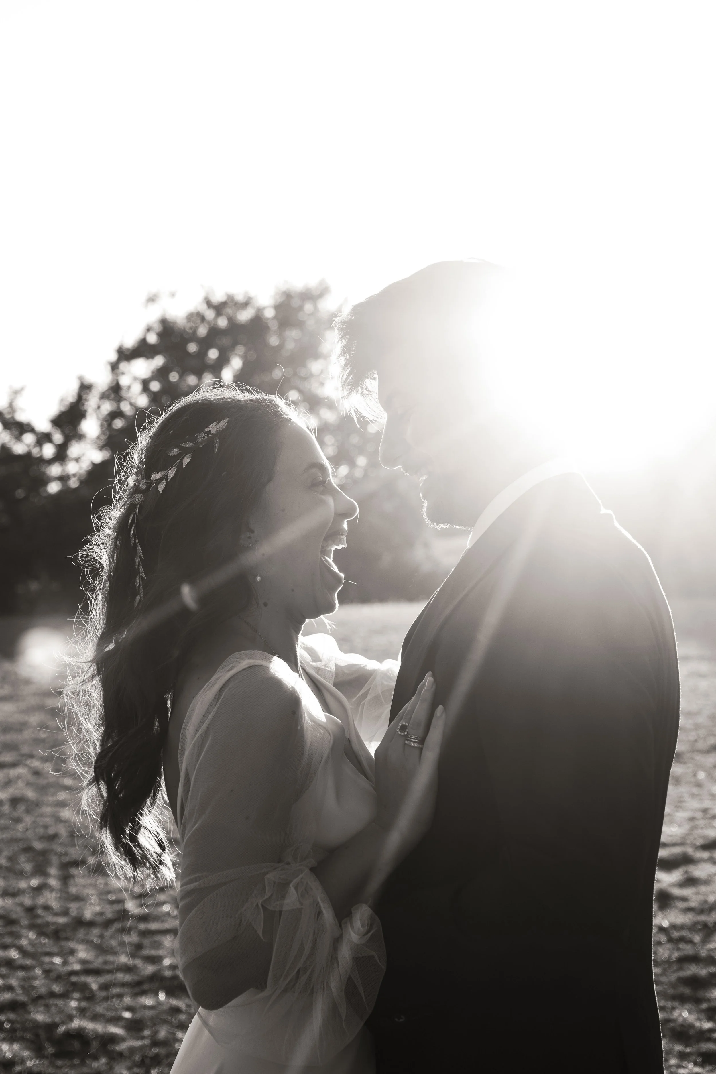 Un couple souriant et heureux en plein air, entouré d'arbres, avec le soleil brillant derrière eux.
