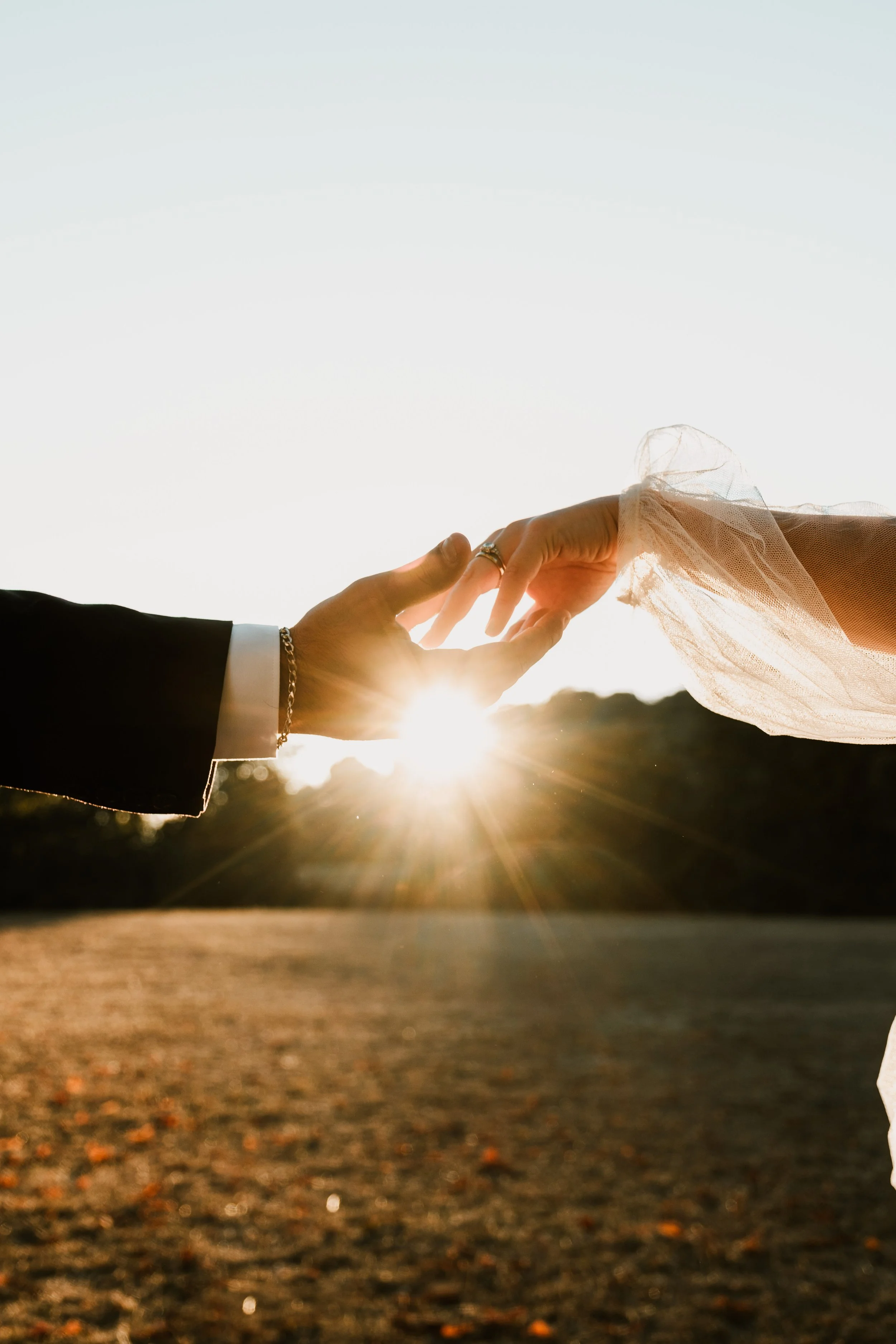 Deux mains se touchent contre fond de coucher de soleil, une main en costume et l'autre en robe de mariée à Grasse