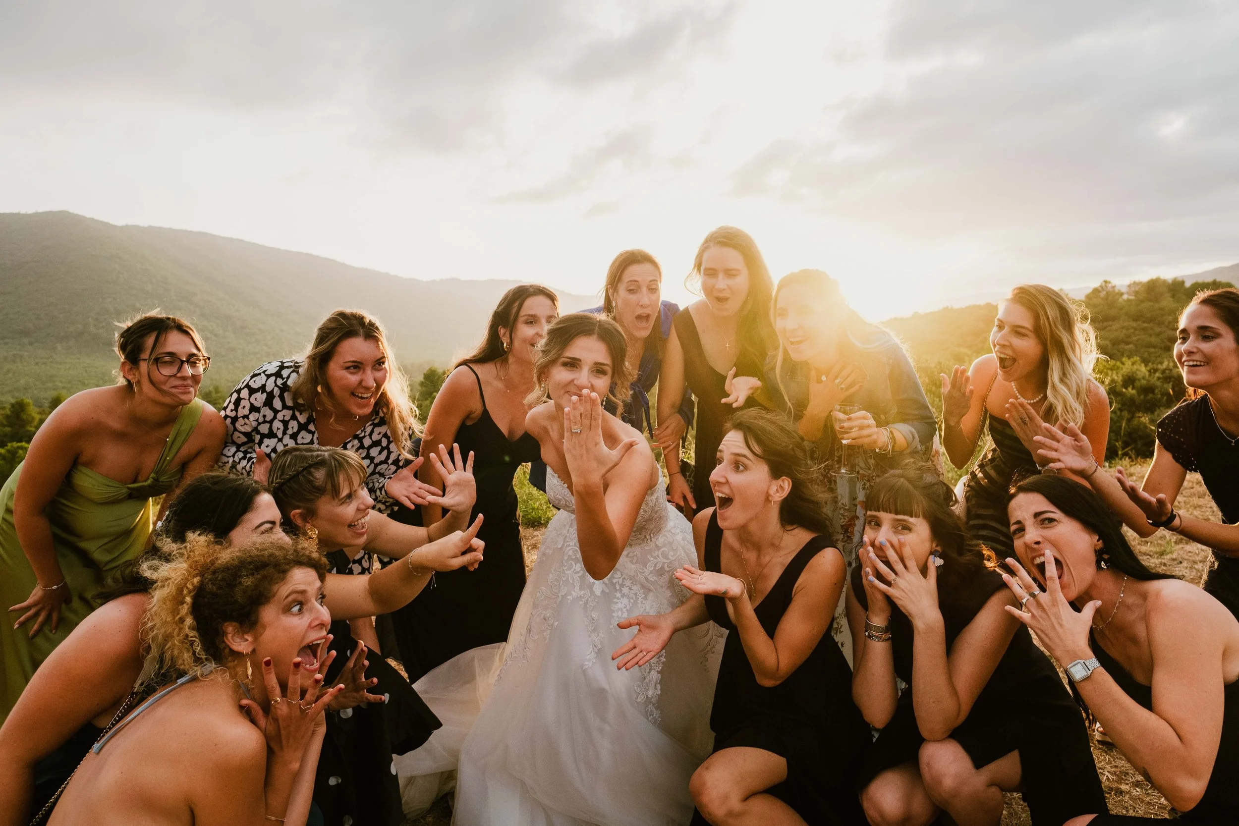 Groupe de femmes célébrant un mariage en plein air avec un paysage de montagnes au coucher du soleil.