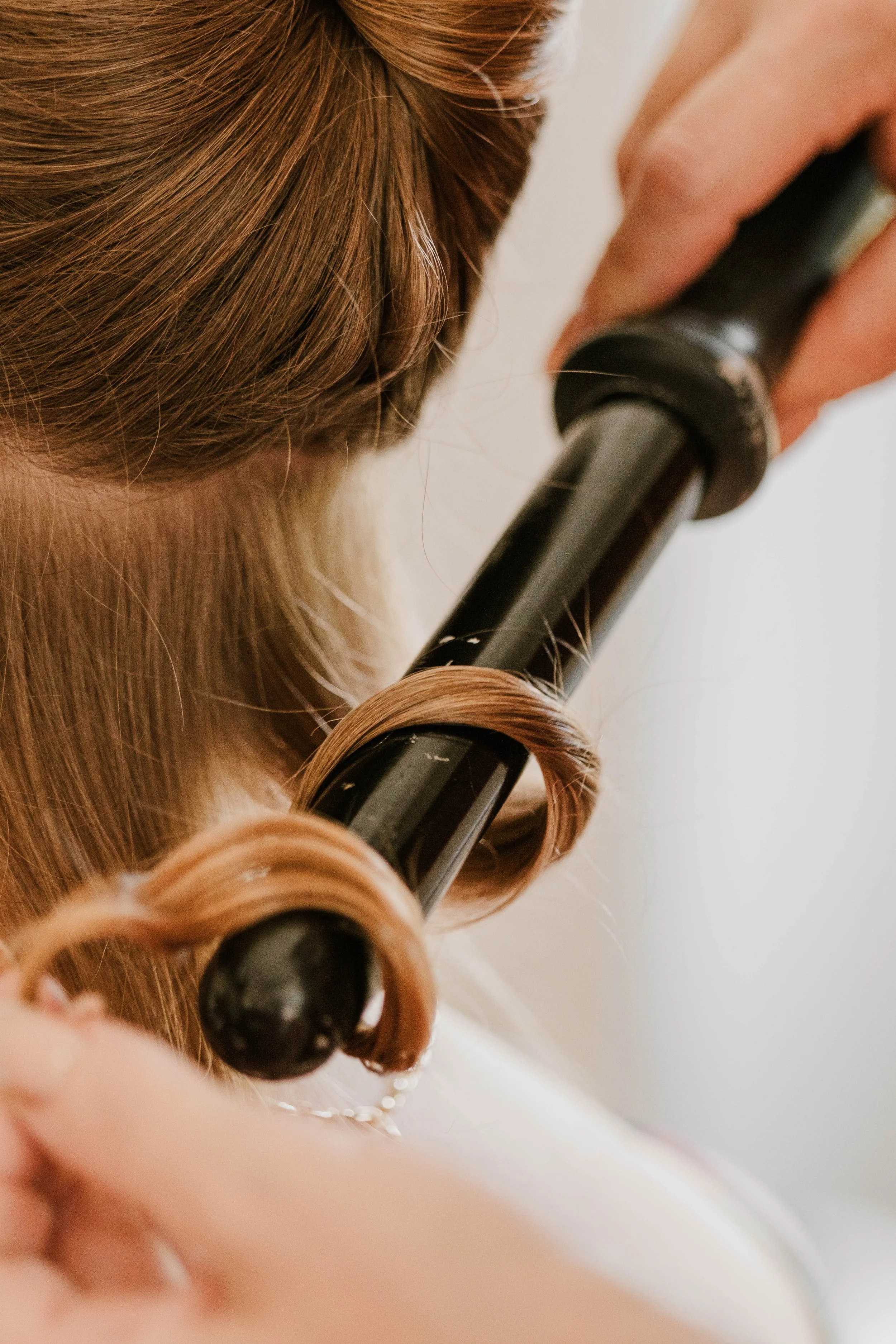 Une personne enroule de la couleur brune dans un fer à lisser ses cheveux.