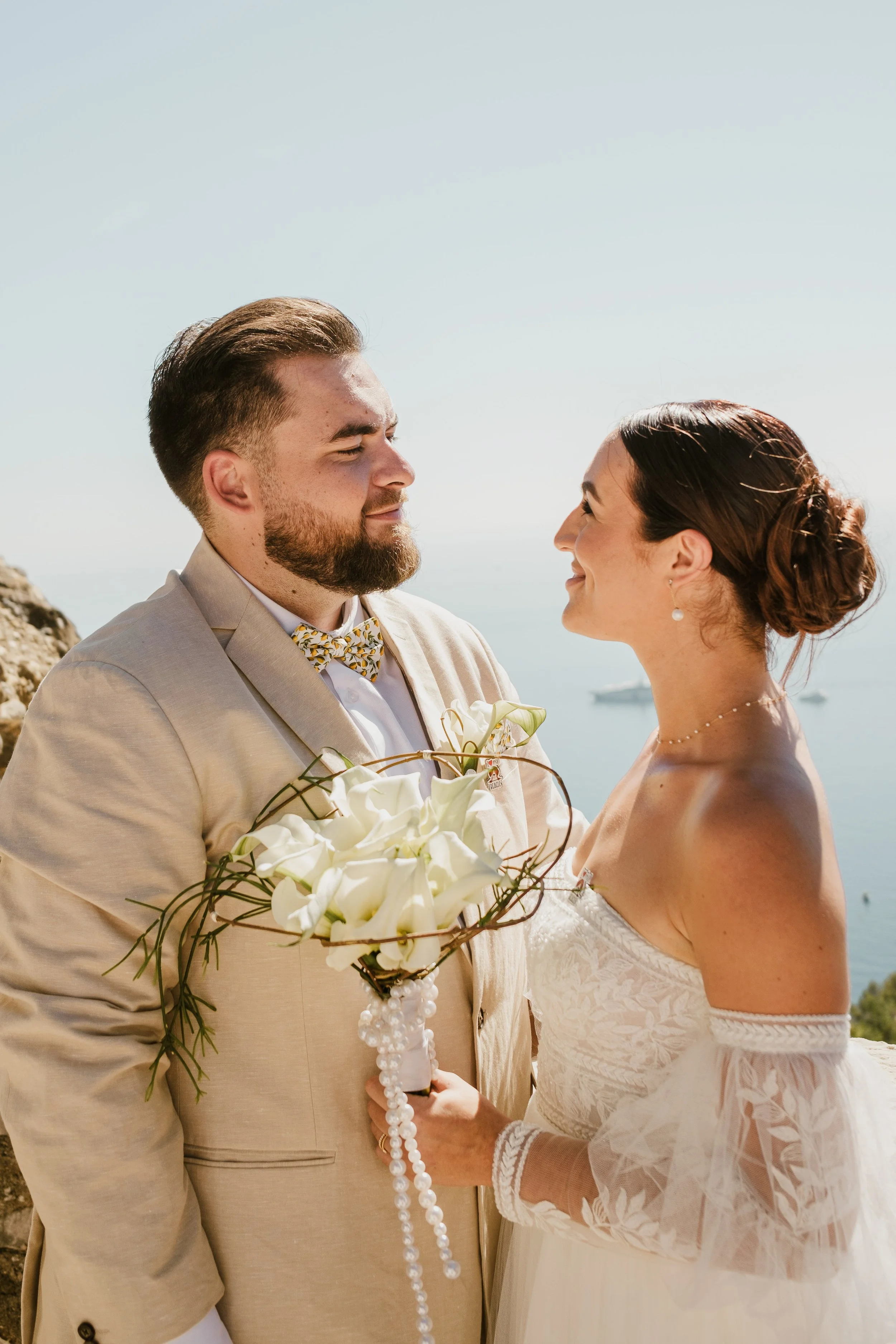 Un couple de mariés regarde dans les yeux lors de leur mariage sur la côte, avec la mer en arrière-plan à Menton.