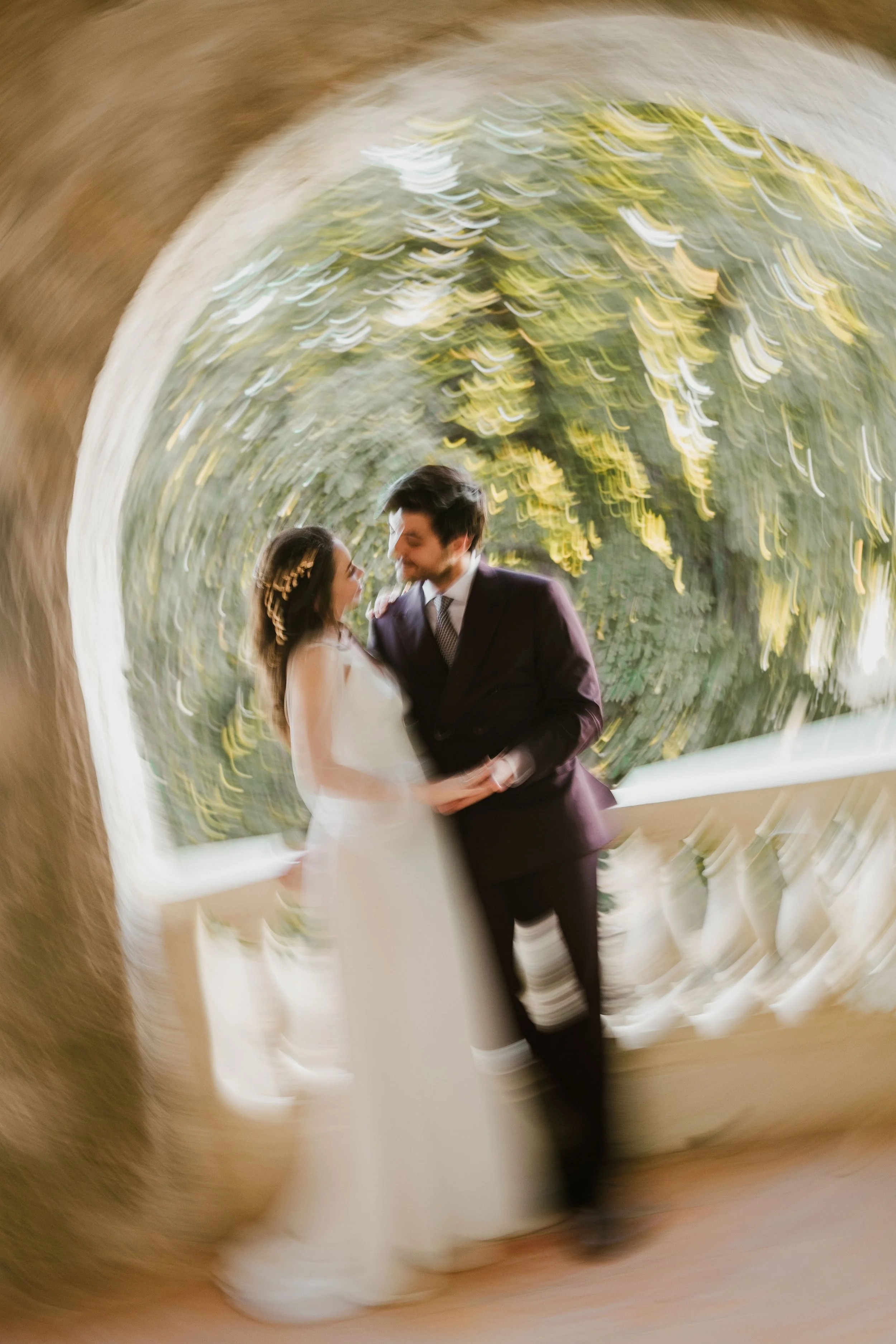 Un couple marié s'embrassant sur un balcon avec un effet de flou artistique autour.