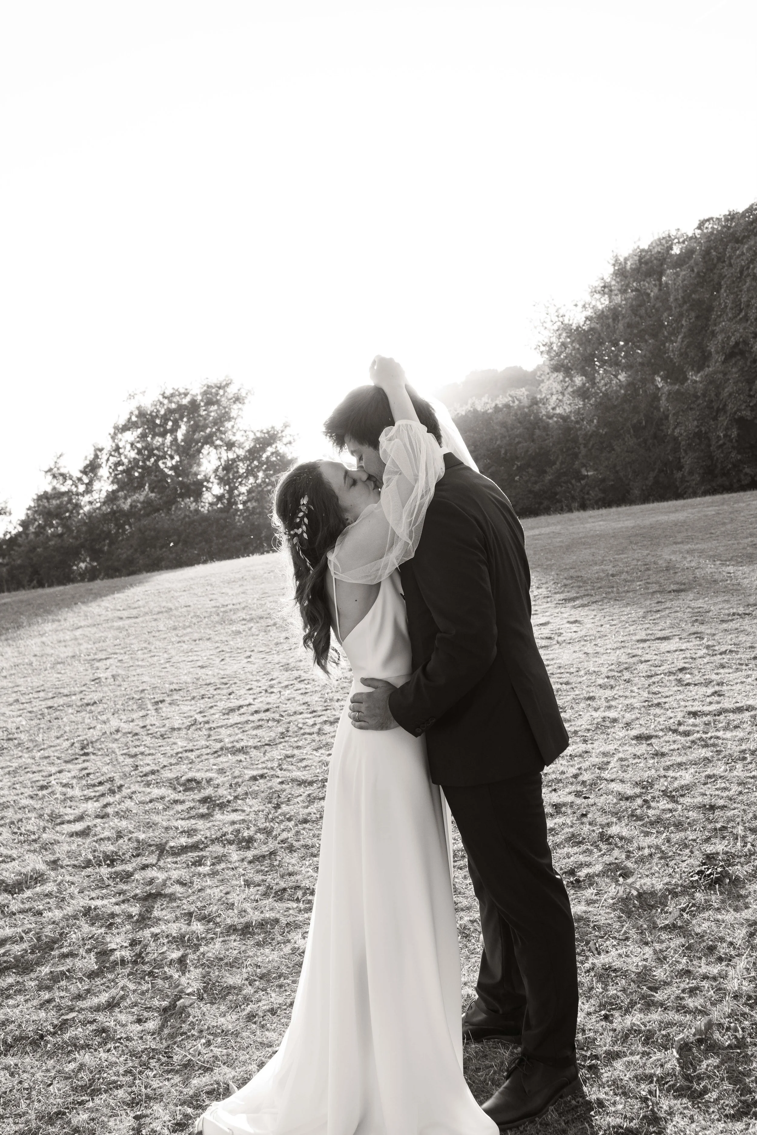 Un couple en robe et costume de mariage s'embrasse dans un champ en plein air, en noir et blanc à Grasse.