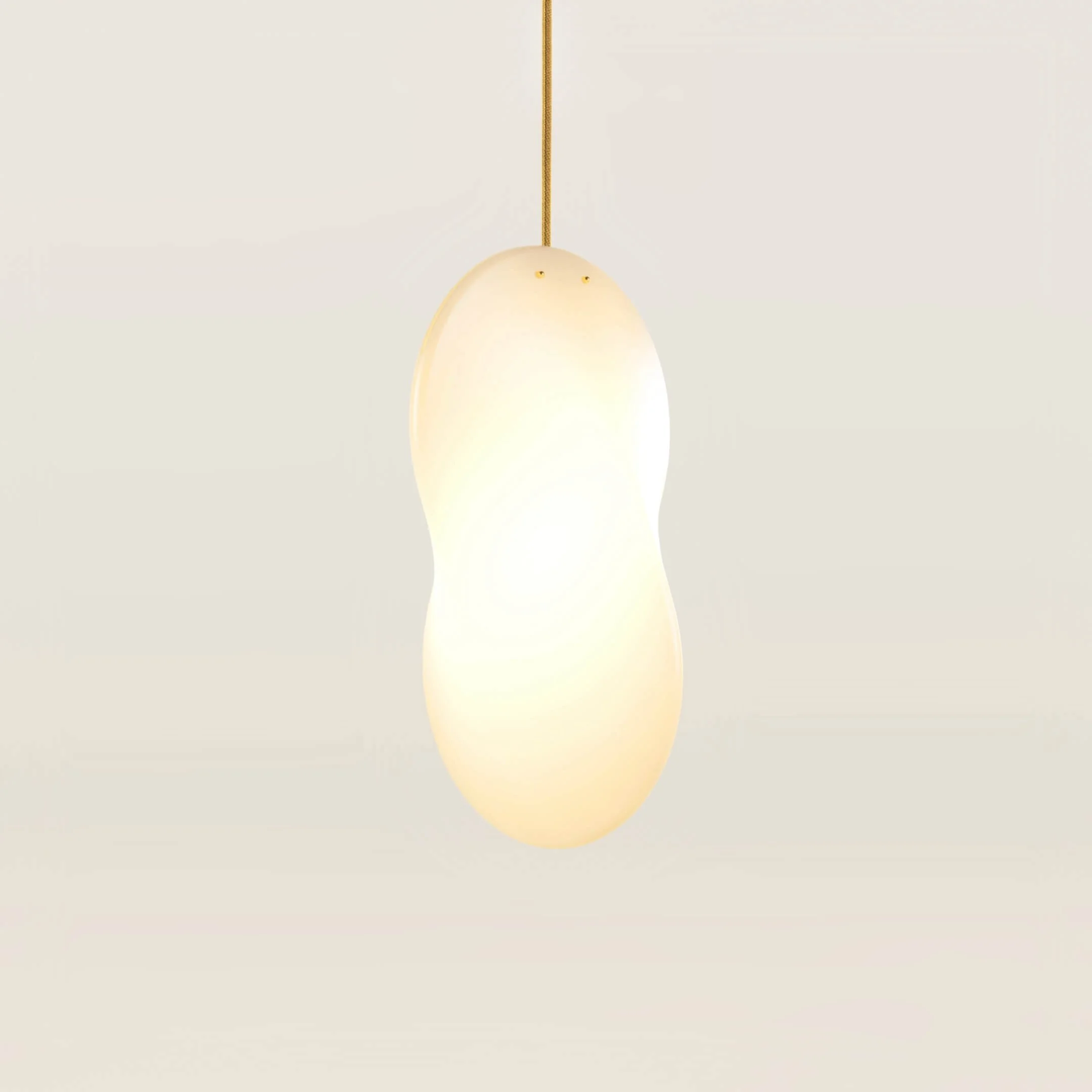 A single Oh Lloyd! pendant light with gold flex and brass fixings. The light is switched on and emits a yellow-orange glow that matches the warmth of the cable flex and fixings.