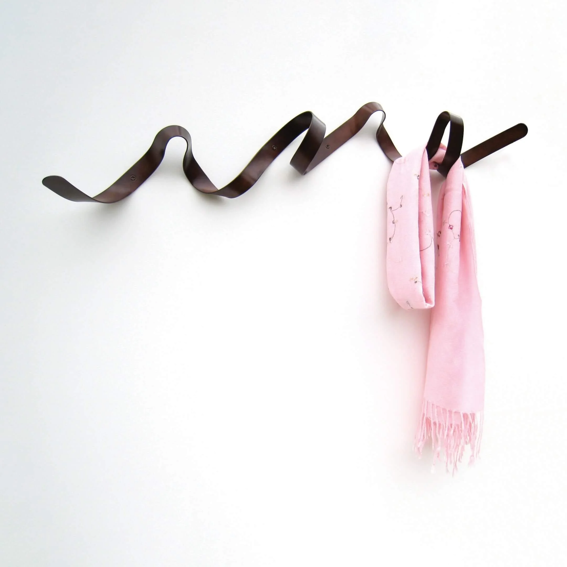 A wall-mounted Ribbon coat rack in weathered bronze. It can hold articles of clothing on each of its loops and bends.