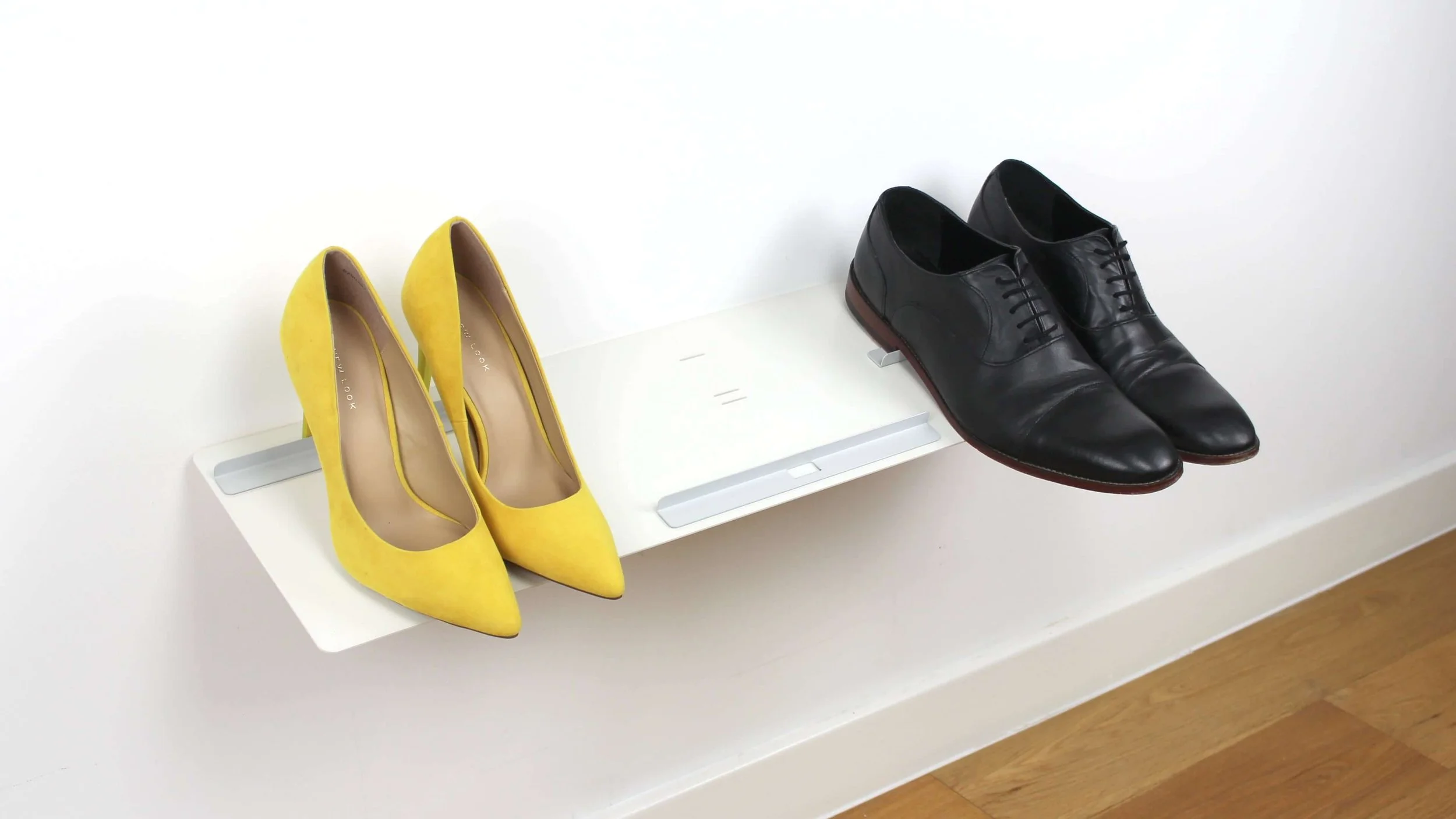 A Versa wall-mounted shoe rack being used to store a pair of women's high heel shoes and men's office shoes.