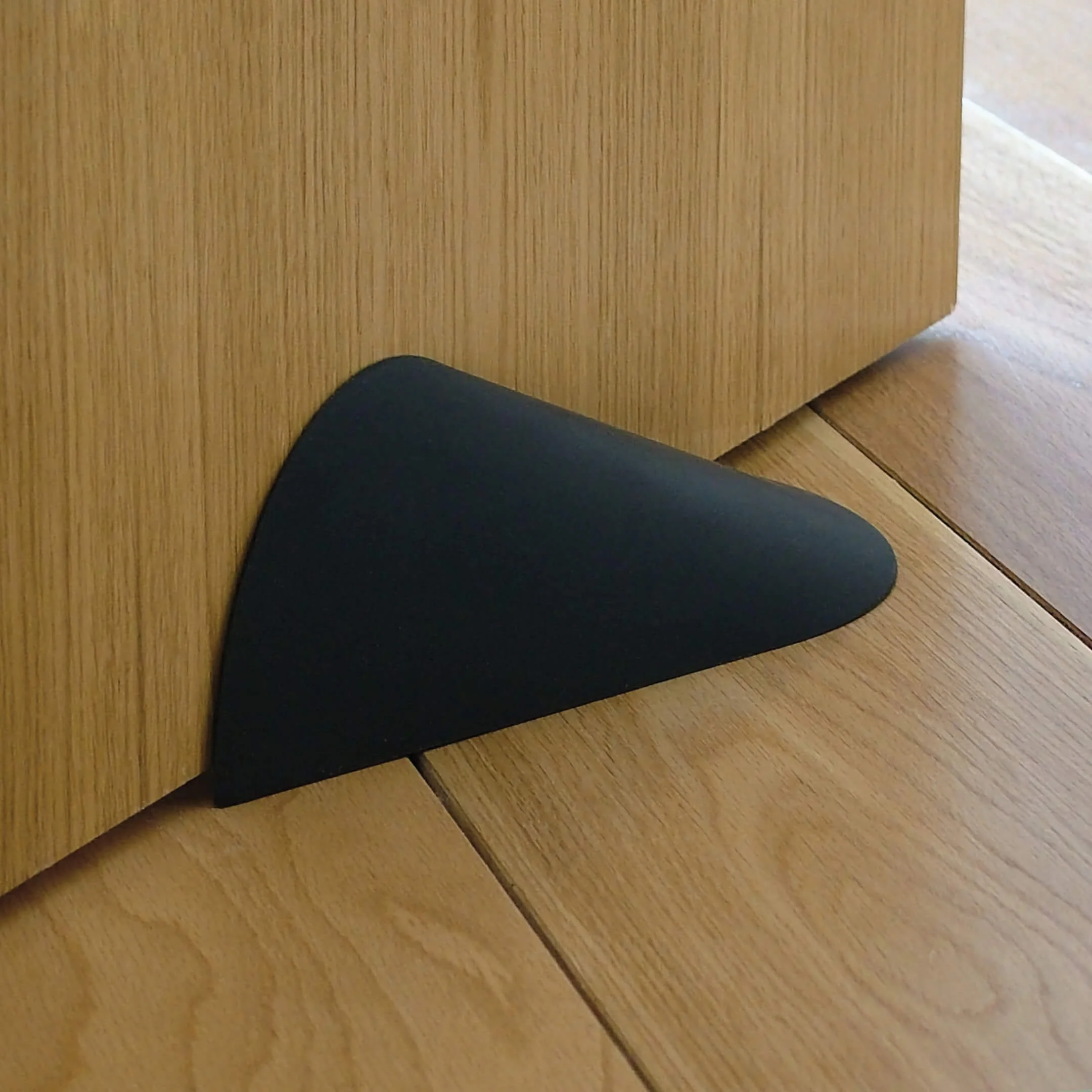A black Ooob being used as a doorstop. Its streamlined form eliminates catch points, so no more stubbed toes.
