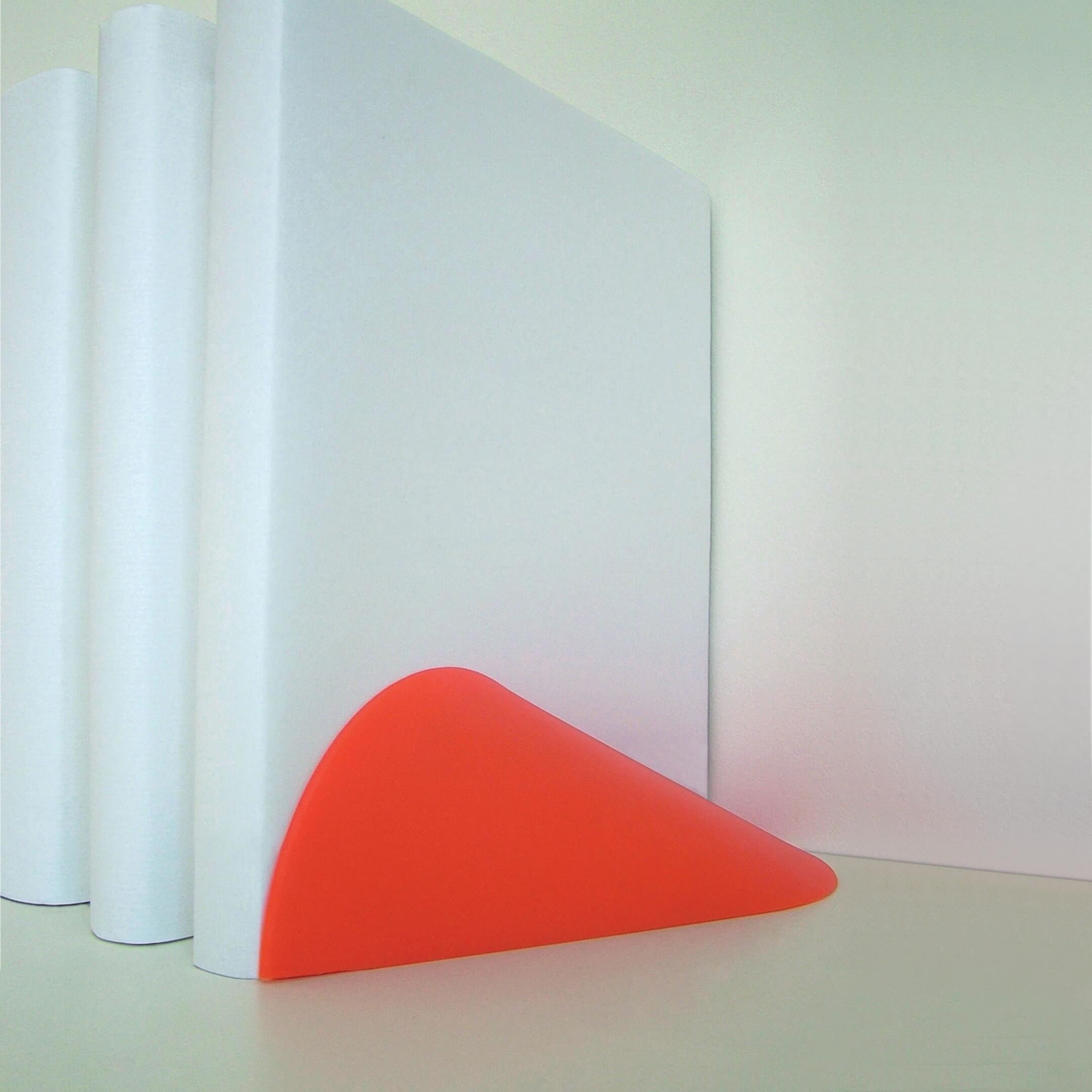 A red Ooob being used as a bookend. Its simple form offers a beautiful juxtaposition against the row of books.