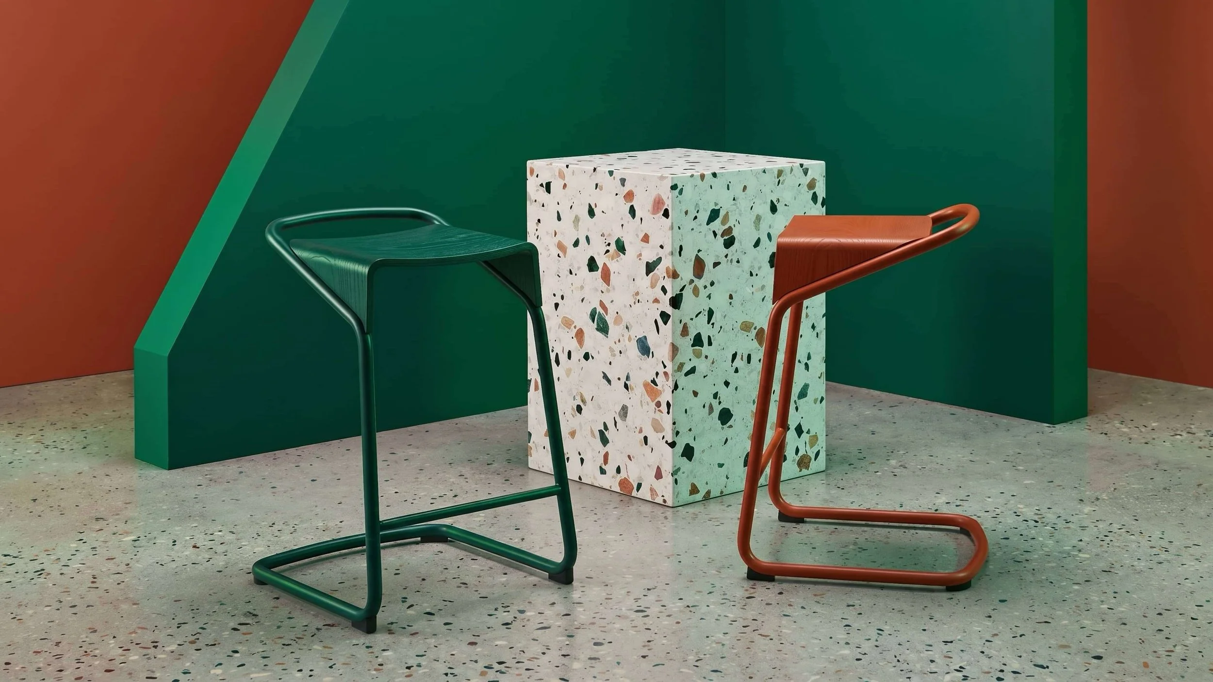Two Camber stools, one in all green and the other in rust orange, in a stylish studio setting.