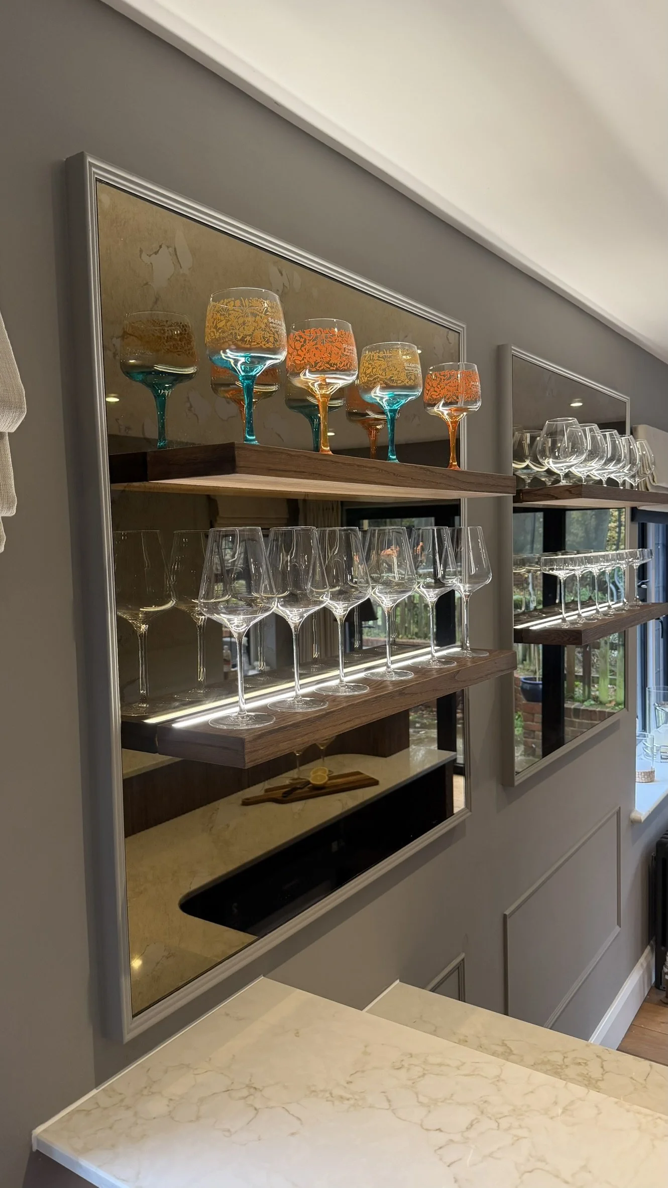 Decorative wall mirror with glassware and colorful glasses on wooden shelves.