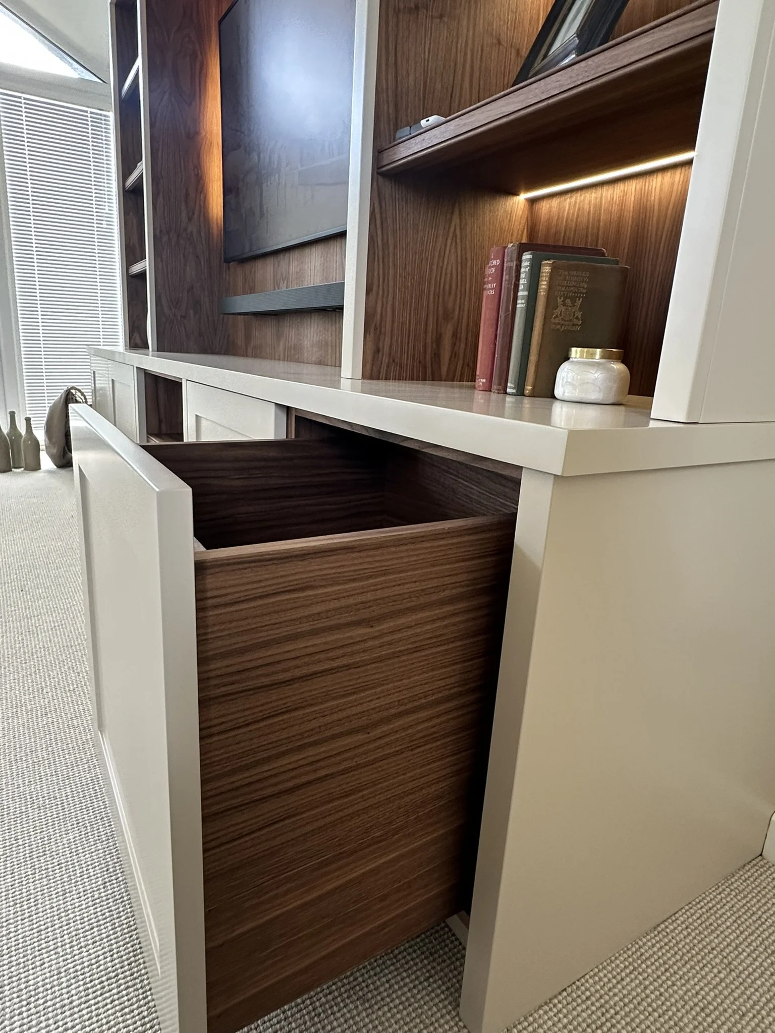 Close-up of a modern living room entertainment unit with open and closed storage, a mounted flat-screen TV, and decorative books and objects on the shelves.