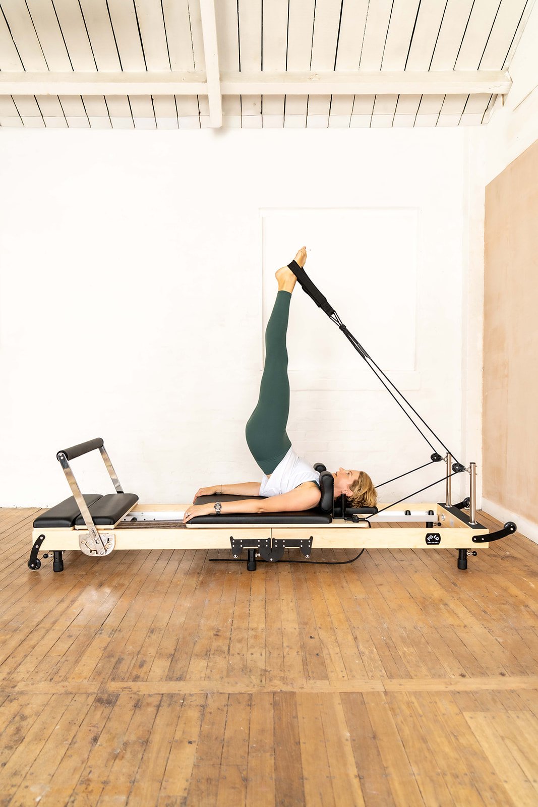 Woman lying on her back on a reformer machine with legs in the air and feet in strapsair