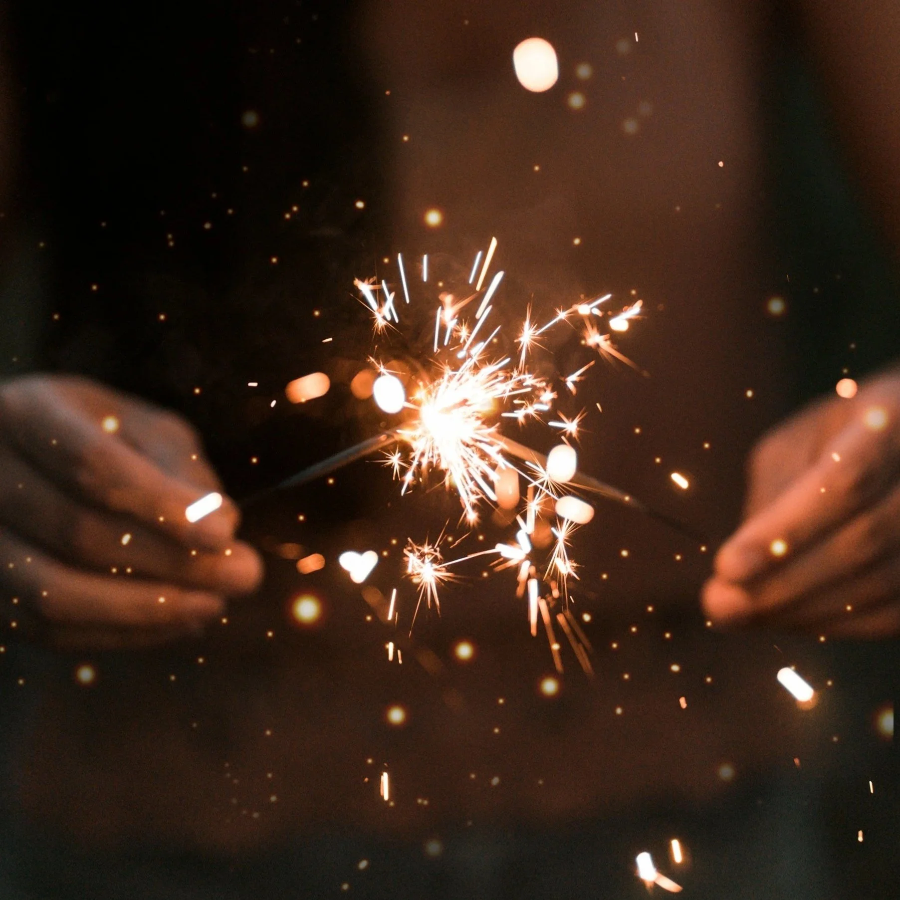 Close-up of a person holding a sparkler at night with sparks flying in various directions, creating a festive and celebratory atmosphere.