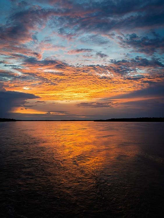 Sunset over a calm river with colorful clouds in the sky.